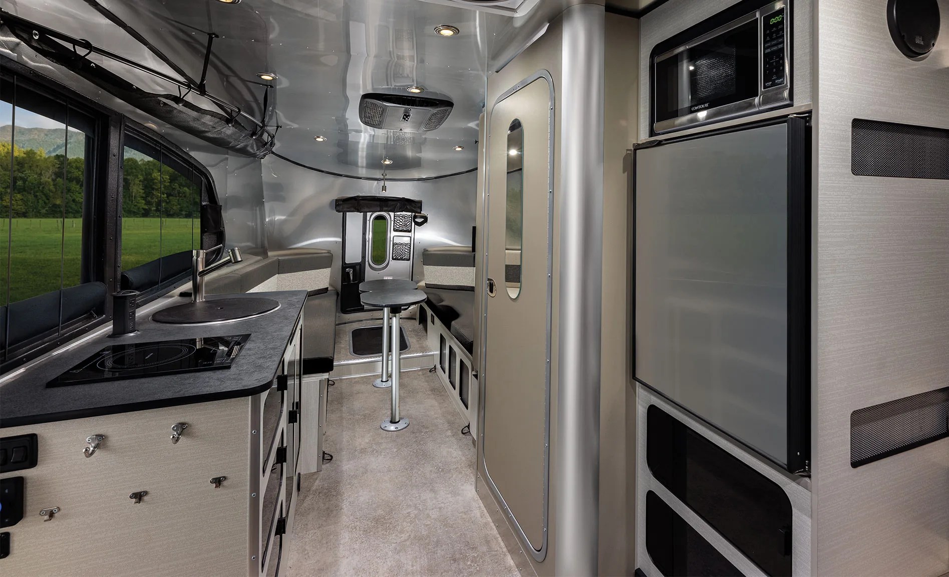 An interior image of the cabin of the Airstream Basecamp Xe trailer showing the galley, rear seating area, fridge and door to the bathroom