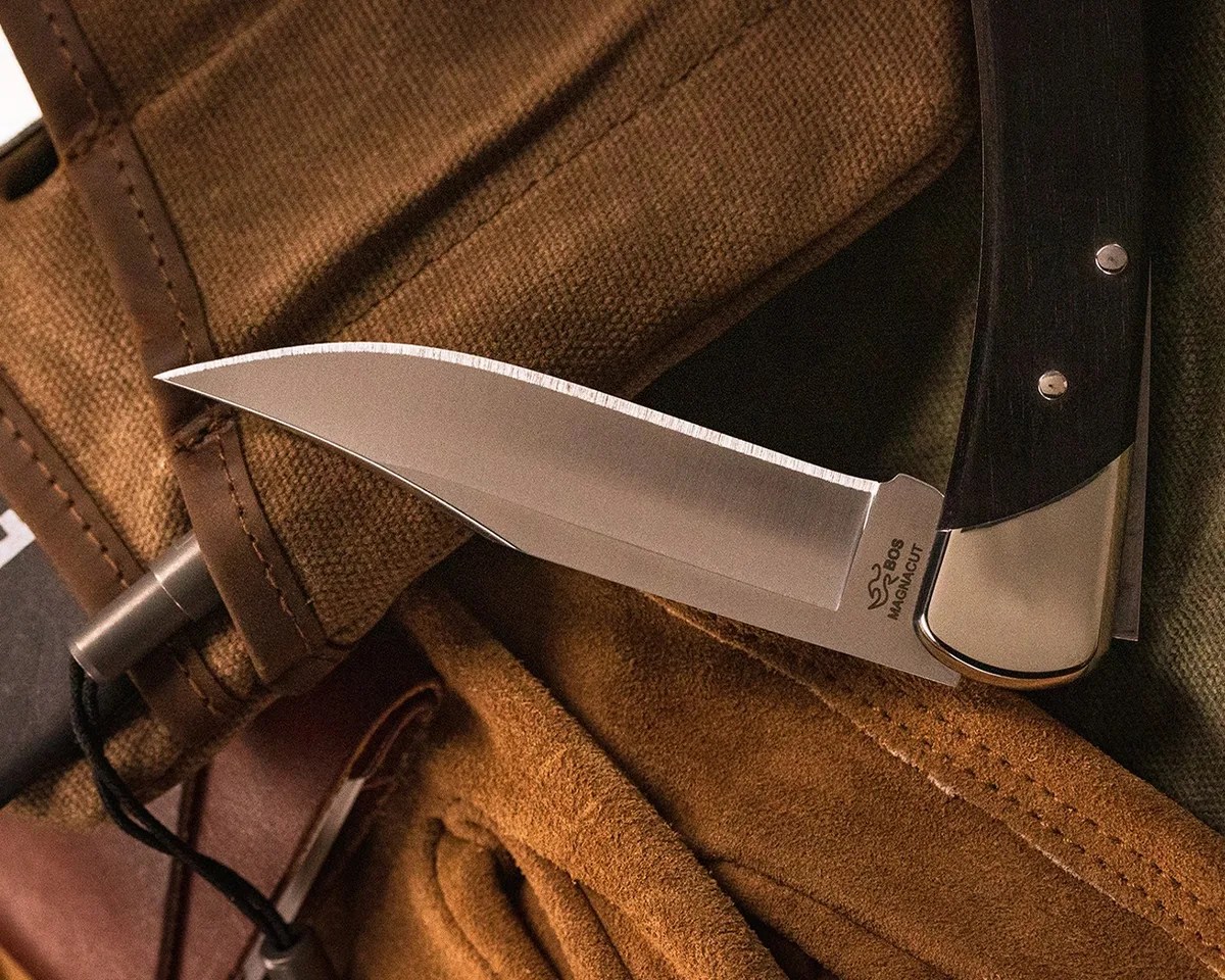 Closeup of Buck 111 Folding Hunter MagnaCut knife blade on nylon EDC pocket above wallet, jacket, valet tray and waxed canvas