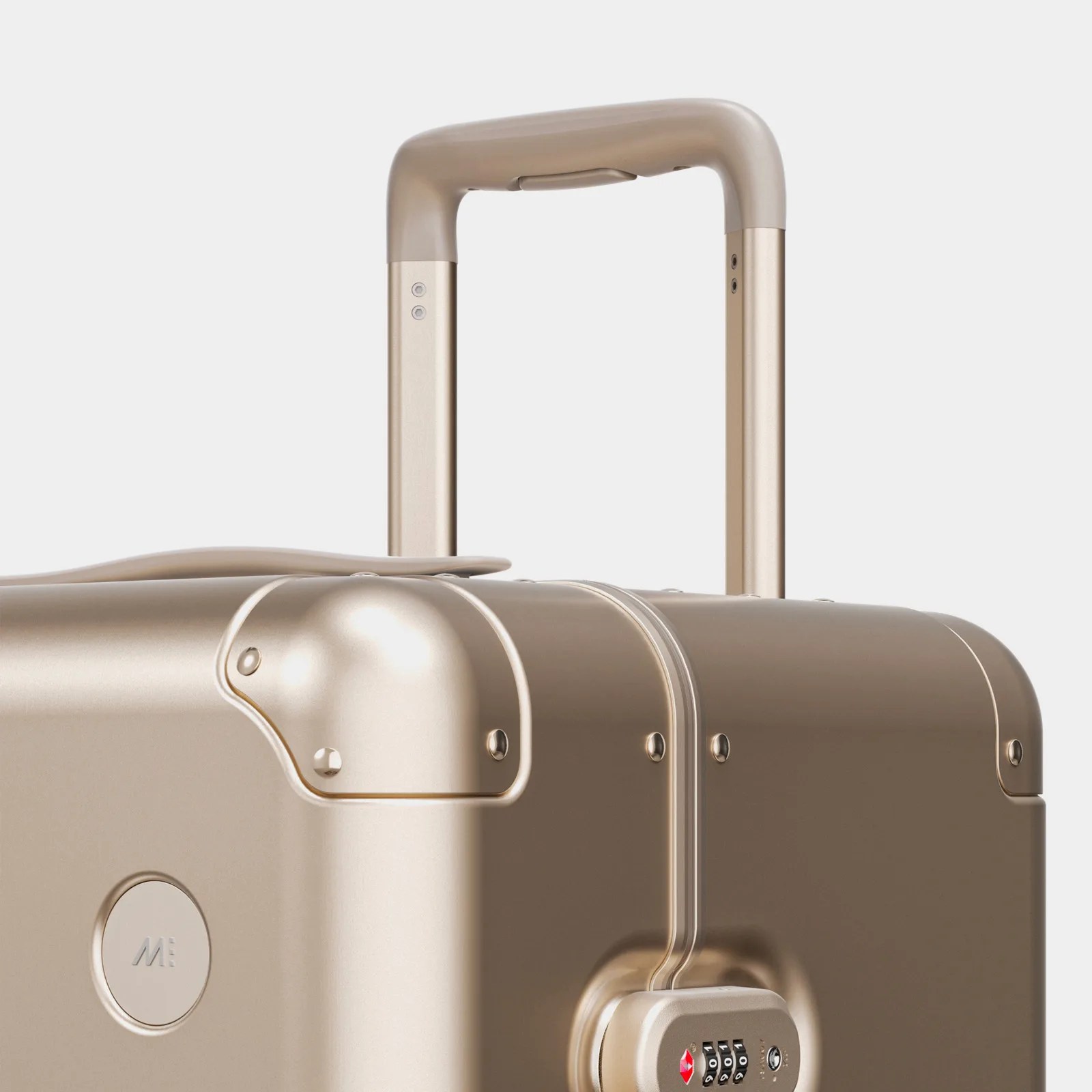 A closeup view of the top and handle area of a Monos aluminum suitcase in champange gold. The upper corner, integrated TSA lock and telescoping handle are highlighted.