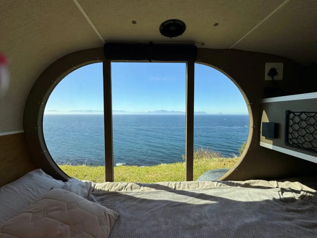A interior view of the Naledi camping view highlighting the adventure trailer's sizeable tinted window, which offers a wide view of the ocean and green grass around the trailer