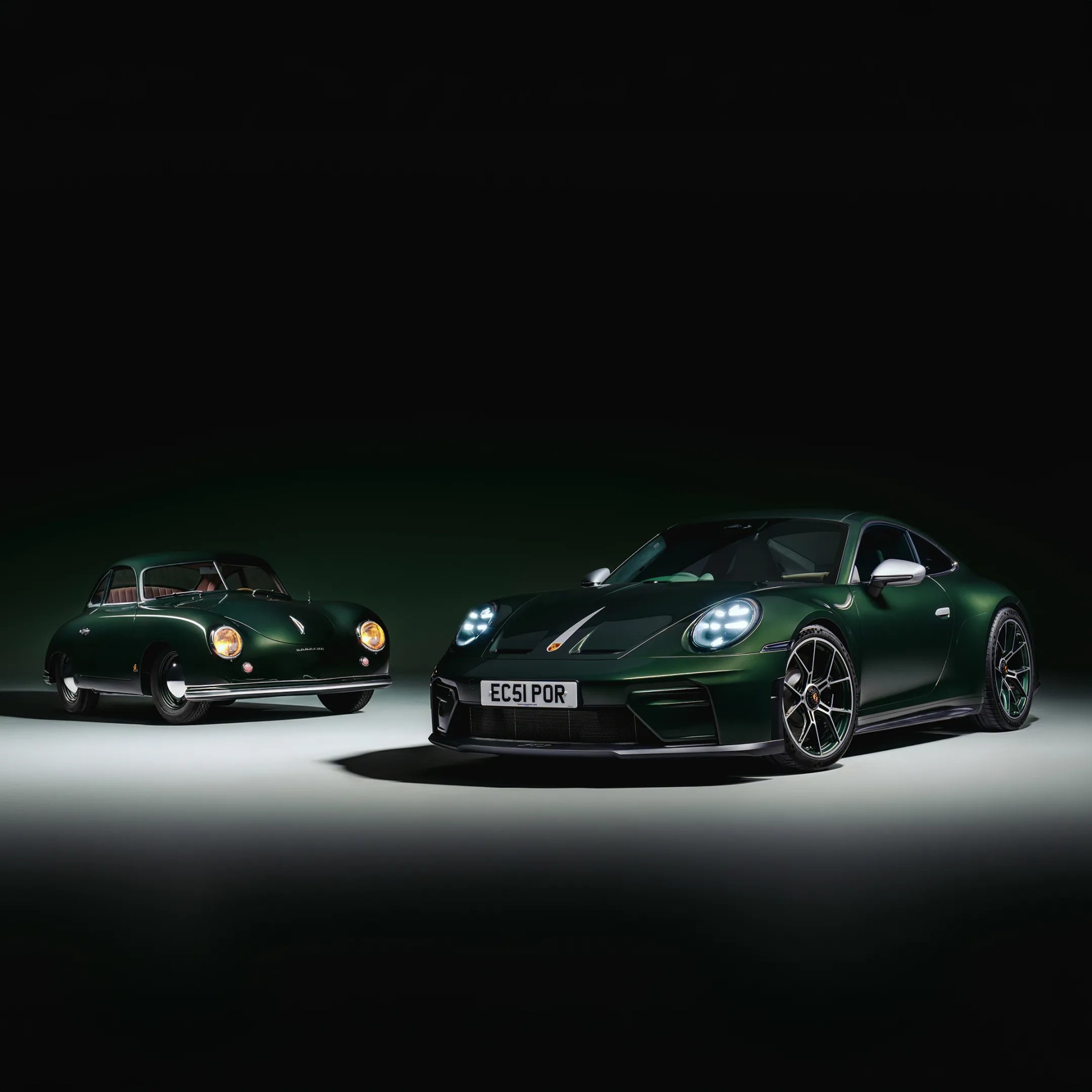 Two dark green Porsche cars, one classic model with yellow headlights and one modern model with bright white headlights, on a dark background.