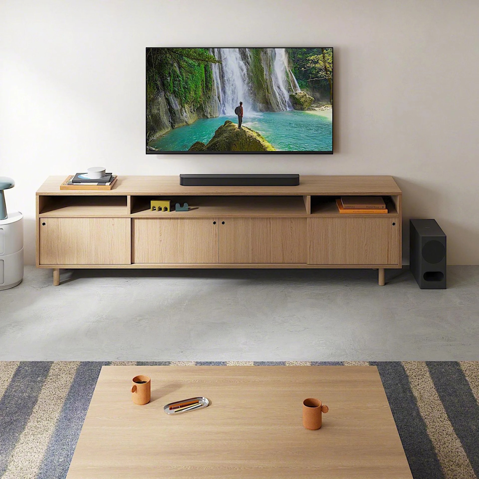 Light wood TV stand with four doors and open shelves, black soundbar on top, and black subwoofer on the floor next to it.