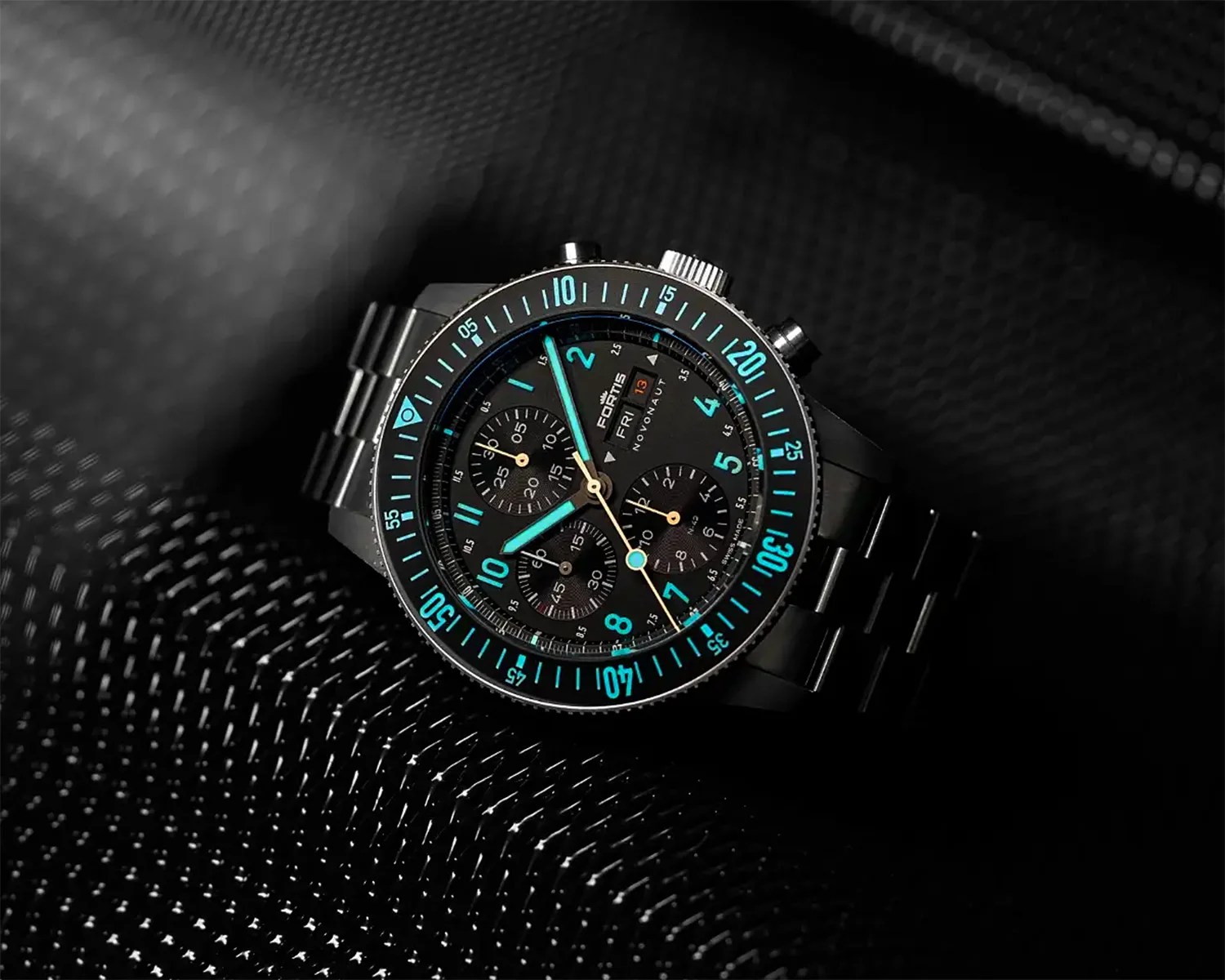 a black chronograph watch in the dark with the lume glowing