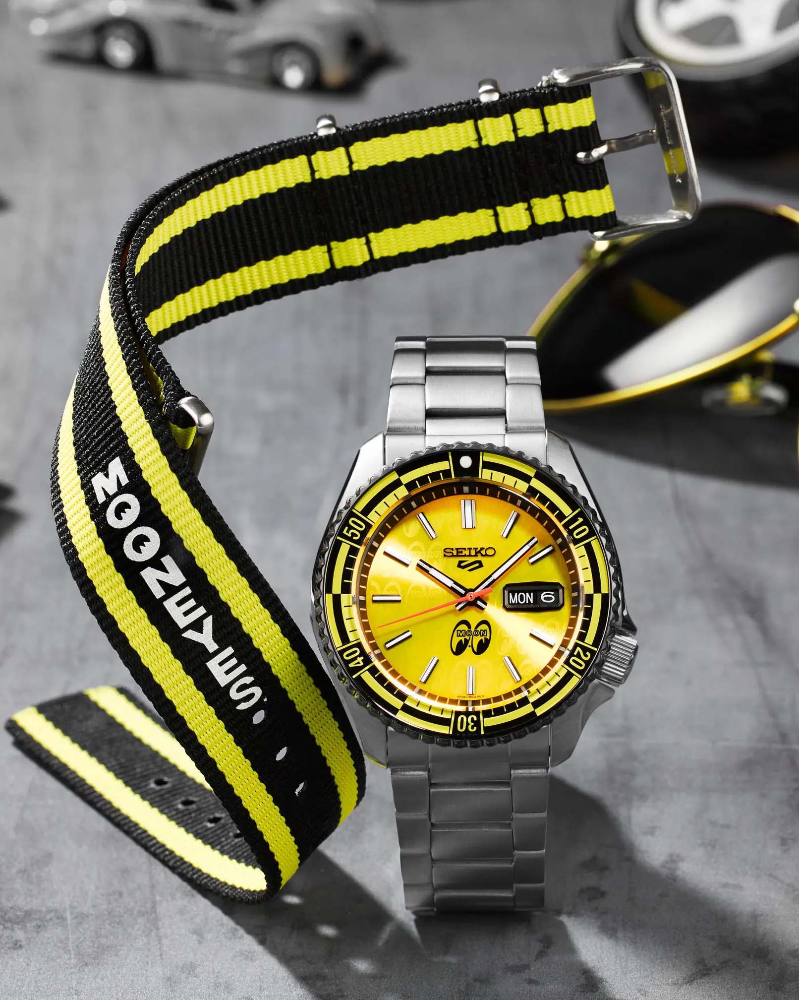 a yellow dial steel sports watch with a black and white nato strap next to it