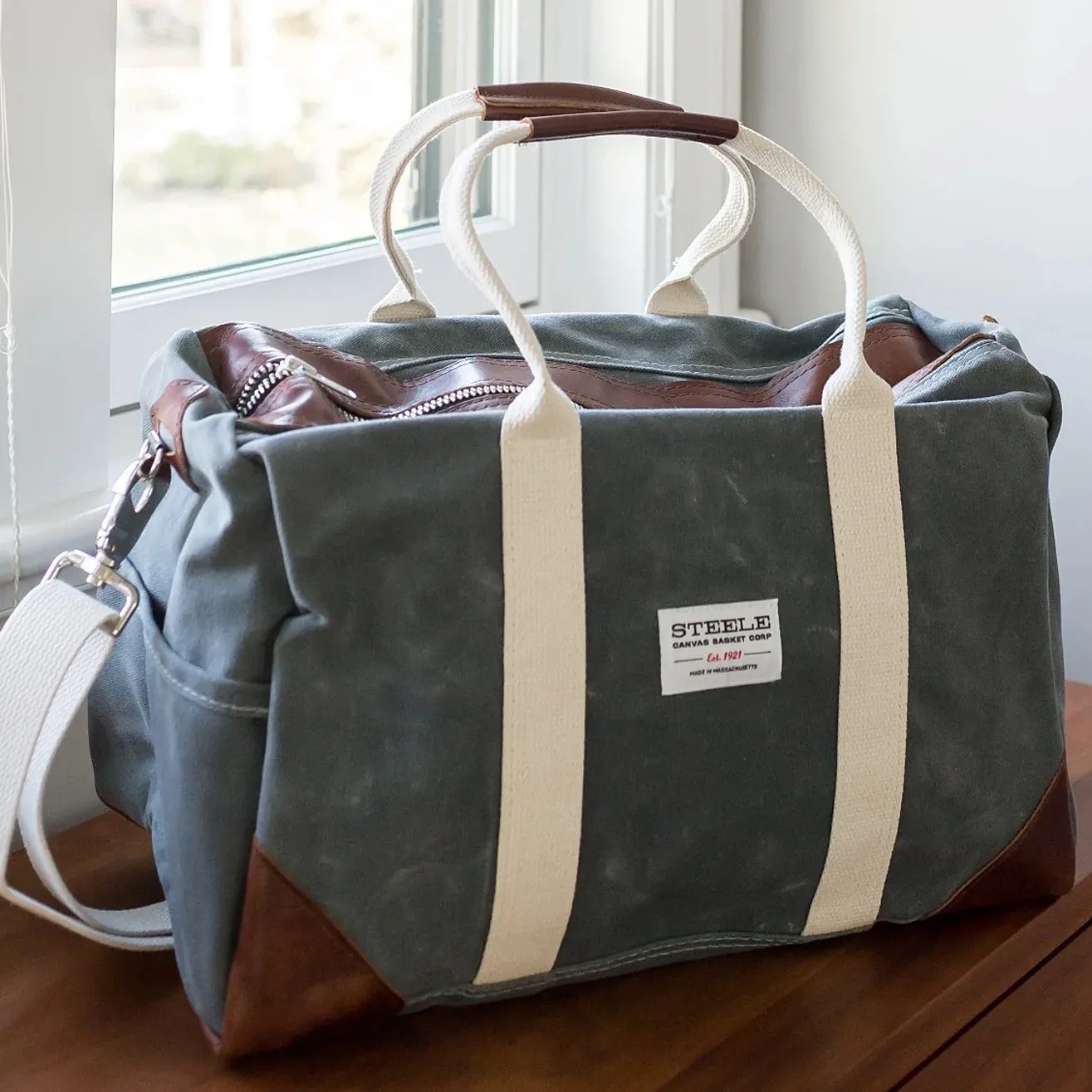 an olive green waxed canvas duffle bag with leather accents