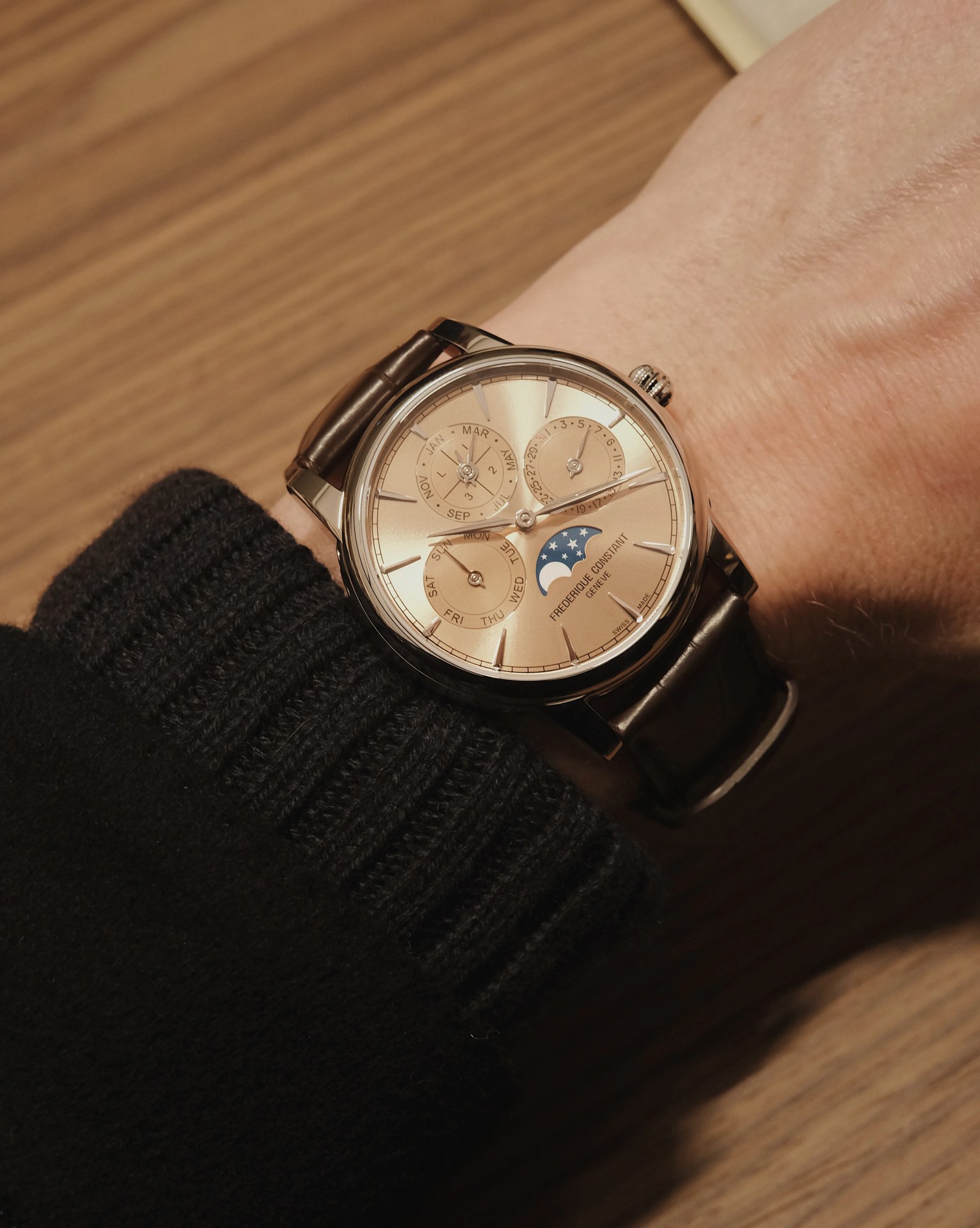 The Frederique Constant Classic Perpetual Calendar Manufacture with a rose gold dial being worn on a male wrist sitting against a wooden desk