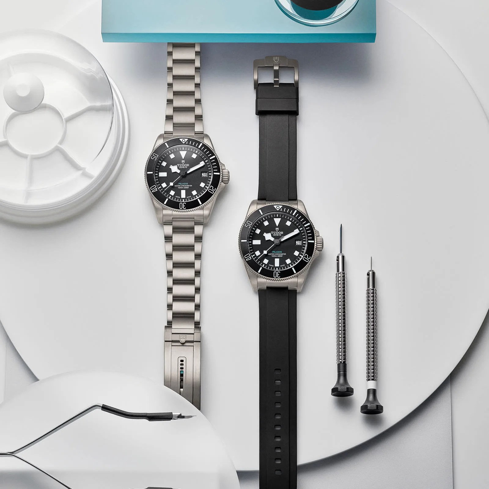 Two Tudor Pelagos Ultra watches, one on a bracelet, one on a rubber strap, shown sitting on a table next to watch strap tools 