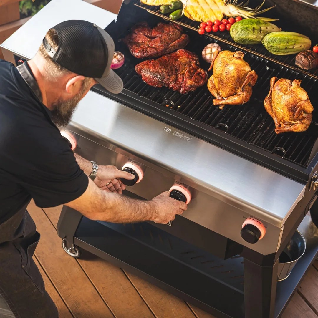 A man bending down to adjust the knobs of the Recteq X-Fire Pro 825, which is filled with chicken, brisket, and vegetables.
