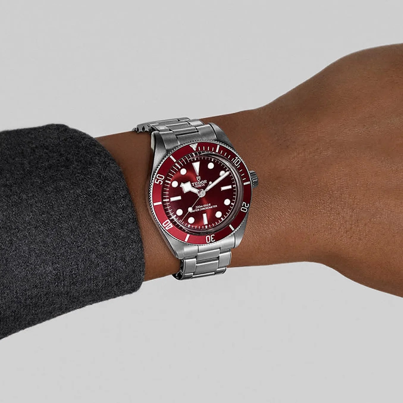 a steel Tudor dive watch with a red dial on a man's wrist