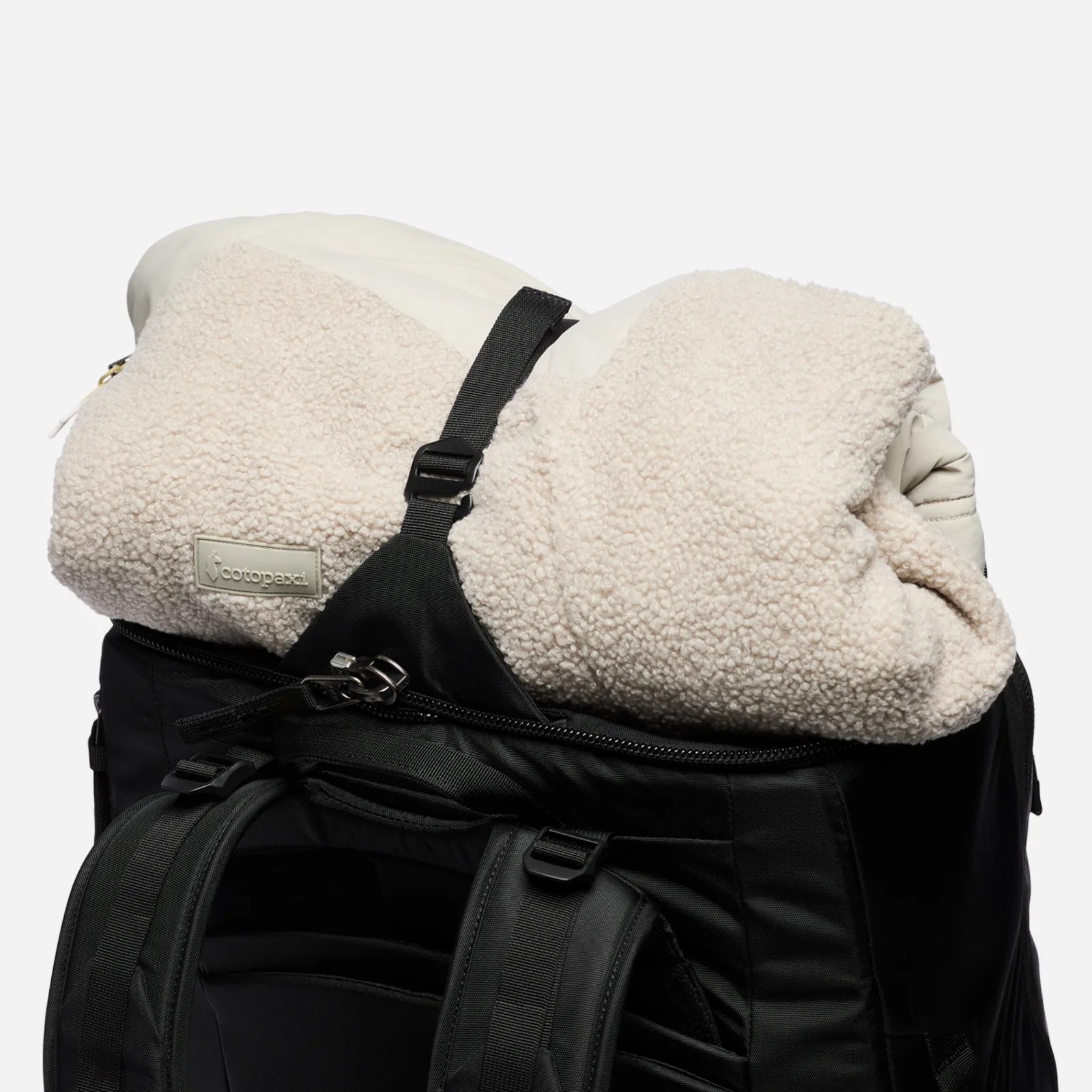 The Cotopaxi Allpa 50L Adventure Travel Pack shown with a fleece rolled on the top of the background against a light grey background
