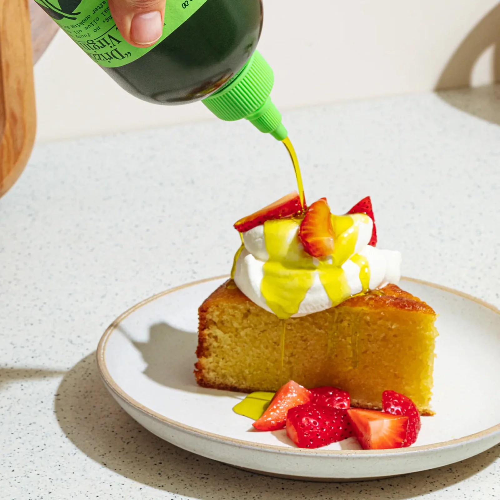 A bottle of Graza drizzle olive oil being poured on a piece of cake with strawberries