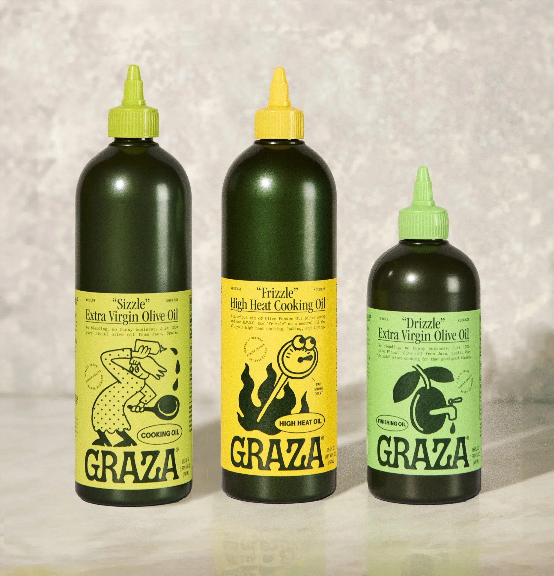 A line up of Graza's three Olive oil products shown resting on a shiny countertop in front of a marbled-looking stone background. 