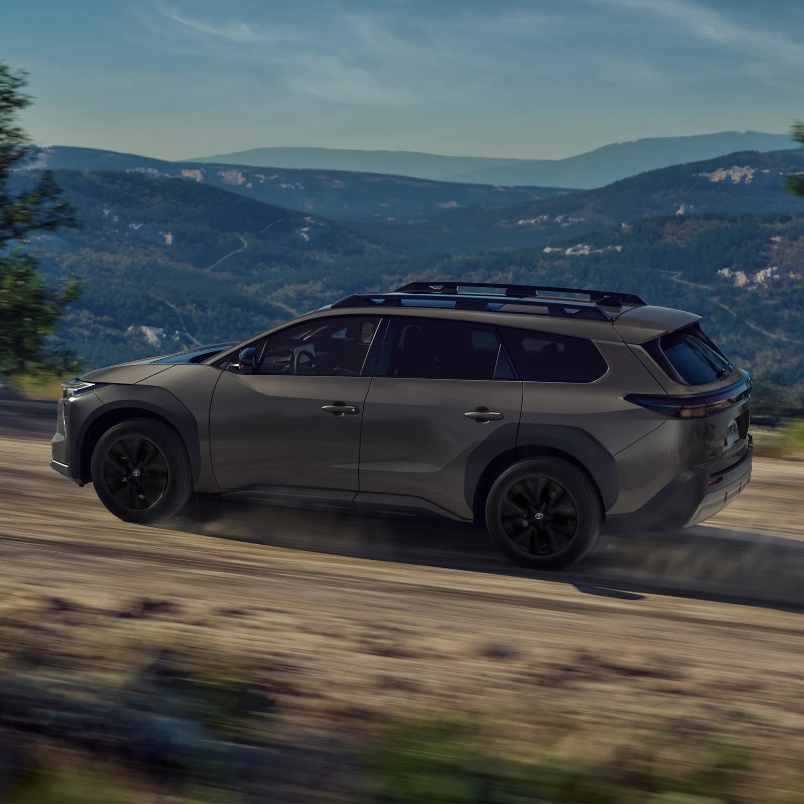 The Toyota bZ Woodland EV shown driving fast in profile along a dirt road with a valley in the distance.