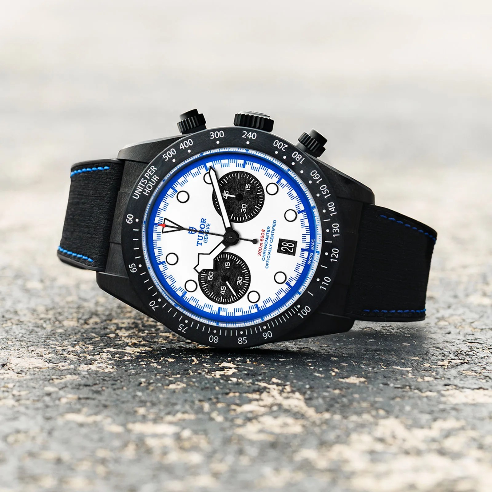 The Tudor Black Bay Chrono "Carbon 25" watch lying on a textured race track on its side.