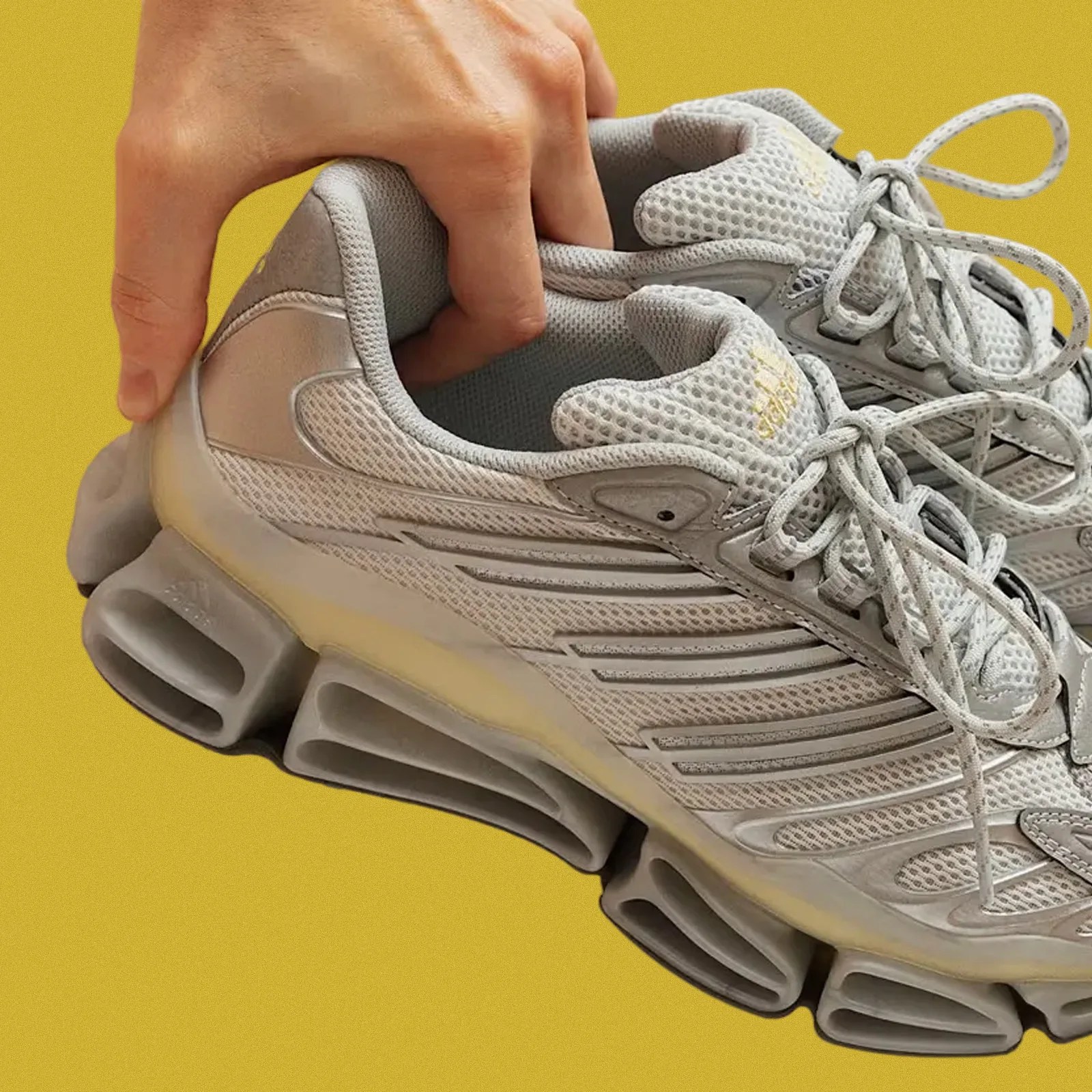 A pair of The Adidas Megarise AG sneakers shown being held by the hells have a single hand