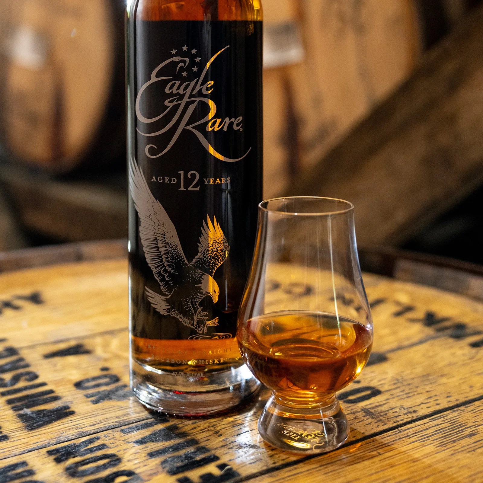 A bottle of Eagle Rare 12 next to a glass of whiskey sitting in a bourbon barrel.