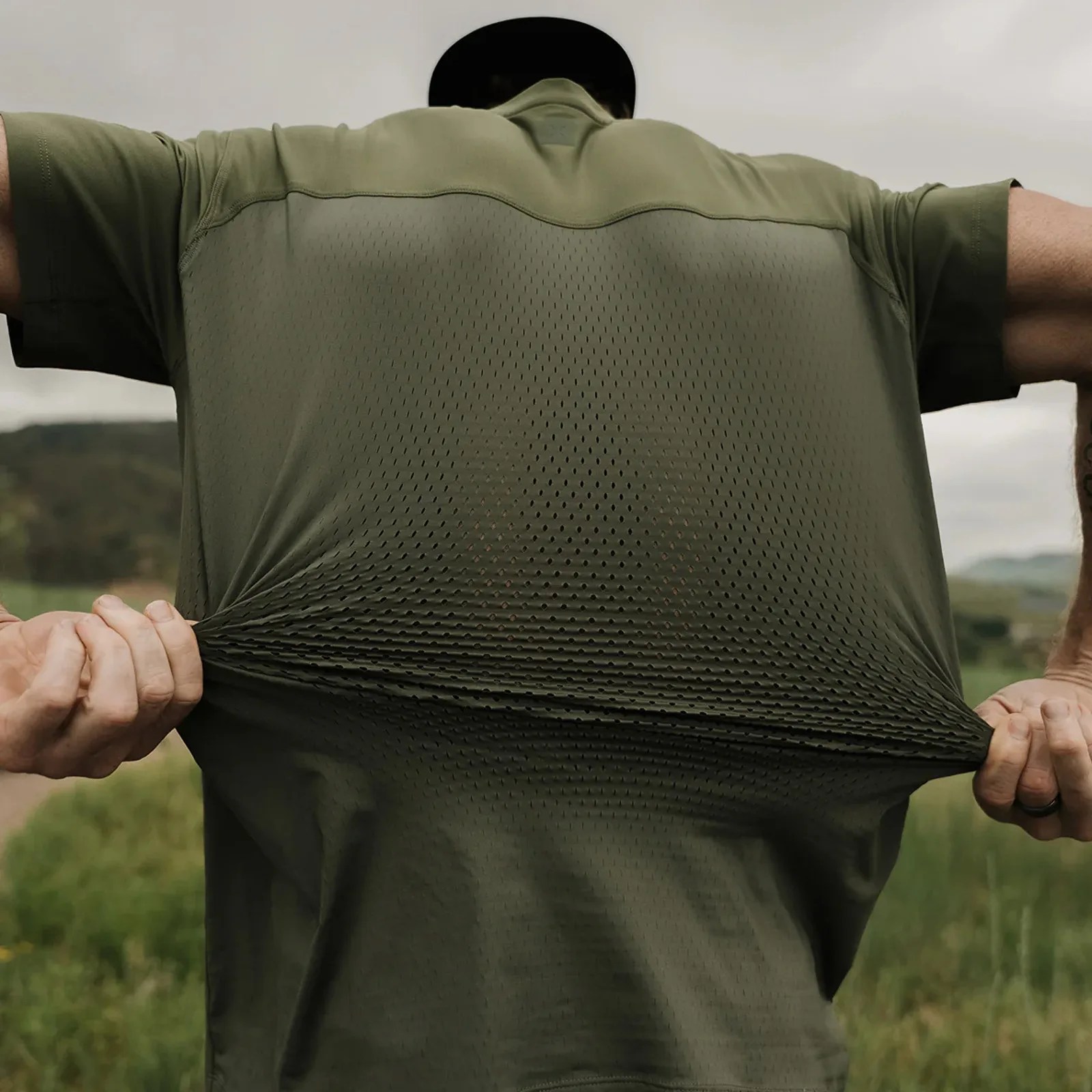 A man shown wearing a Ten Thousand Tactical recon shirt shown from the back using his hands to stretch the back to reveal the ventilated holes