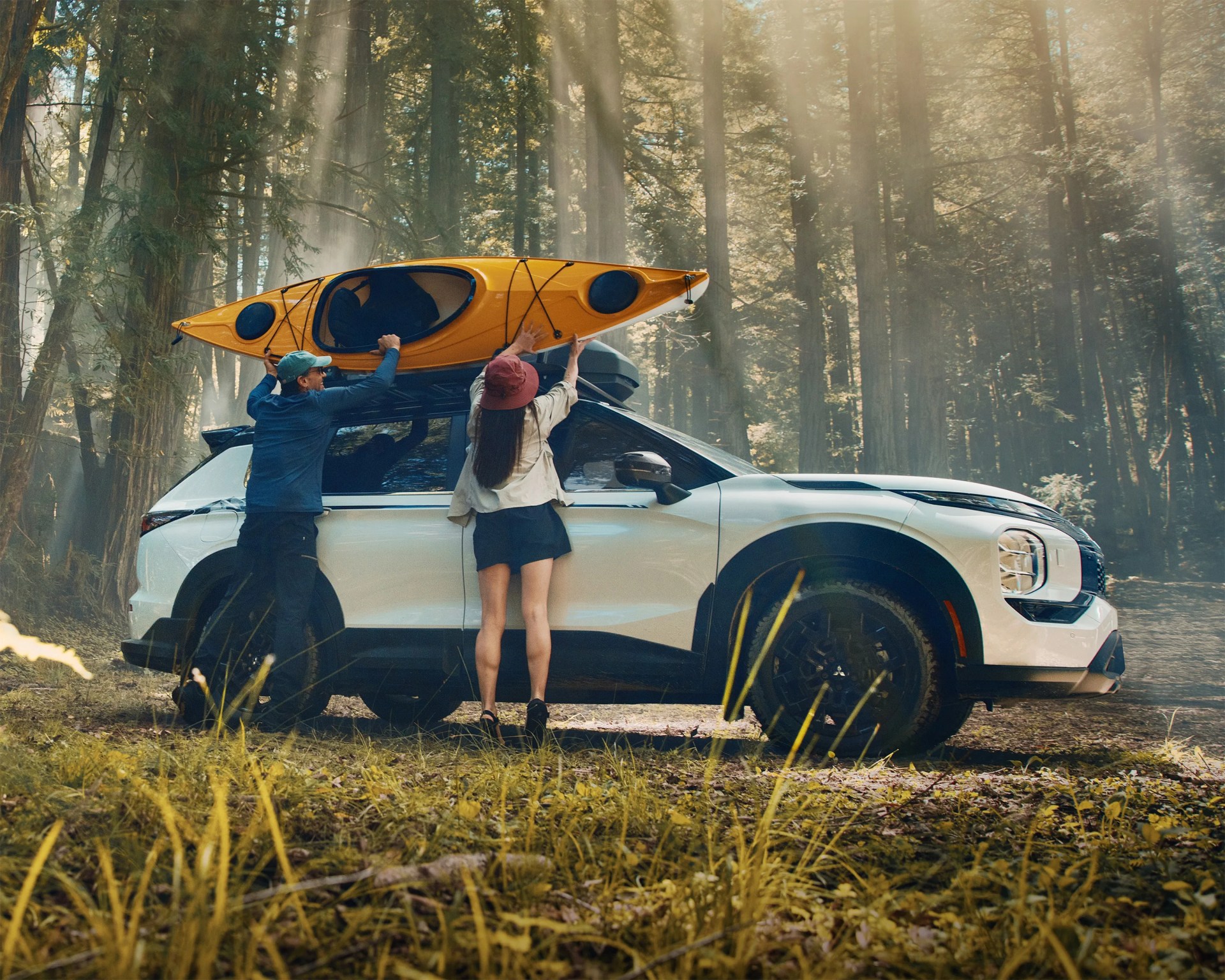 a photo of a white mitsubishi suv with a yellow kayak on the roof