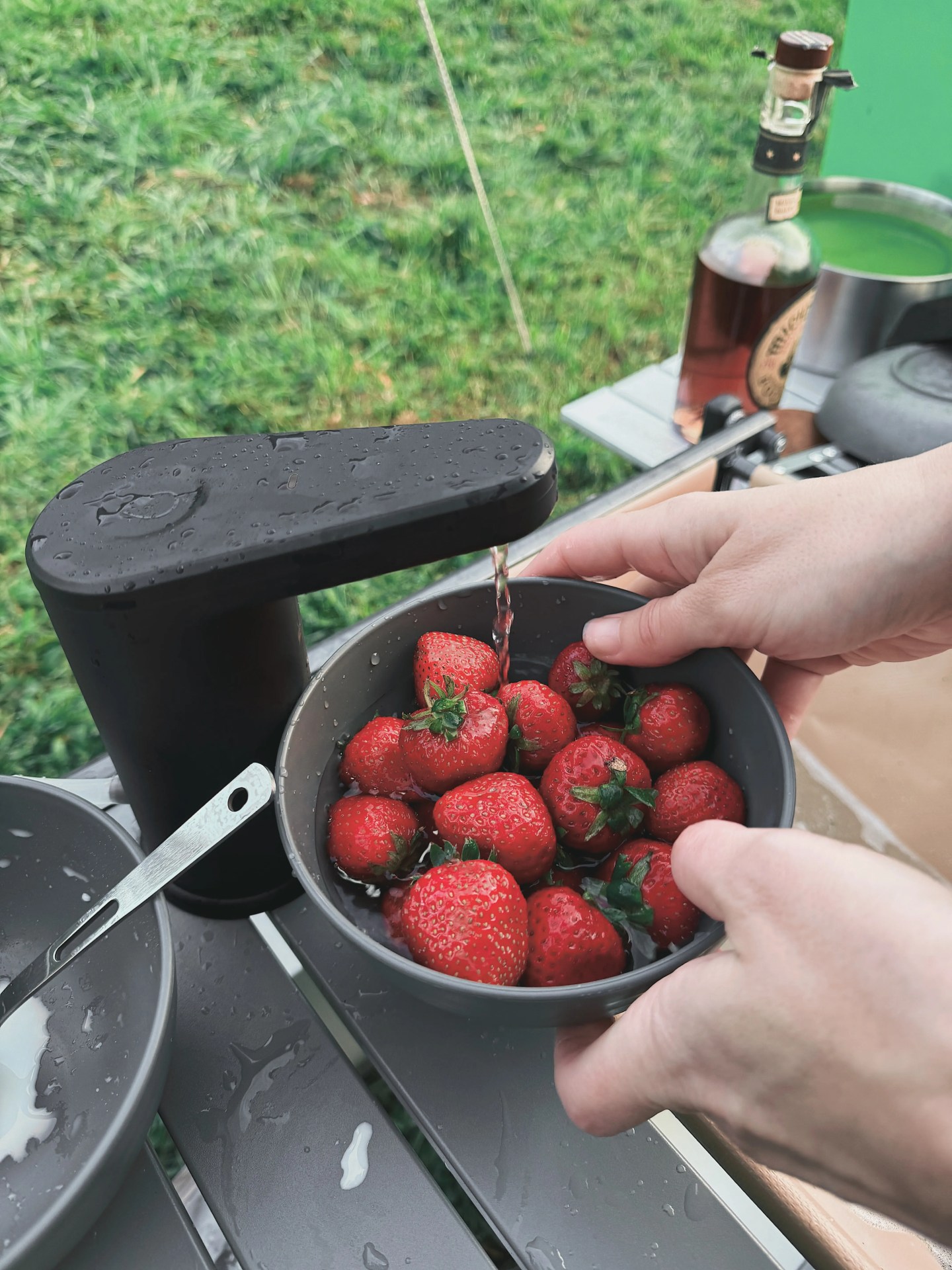 The Dometic Go Hydration Water Faucet shown being used to rinse a bowl of strawberries in a camp kitchen
