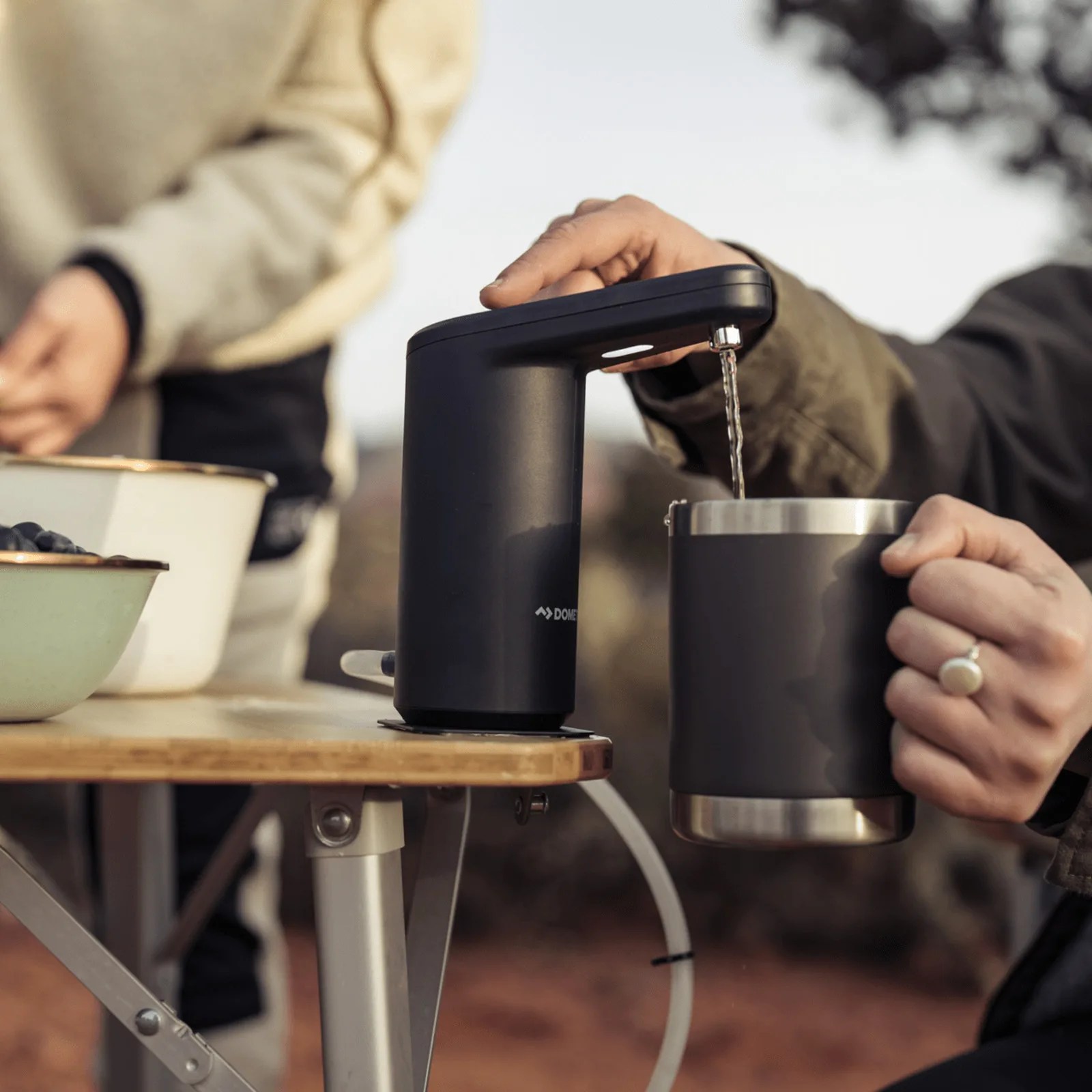 The Dometic Go Faucet shown from the side being activated by a finger and pumping water into a black camp mug held in a campers hand