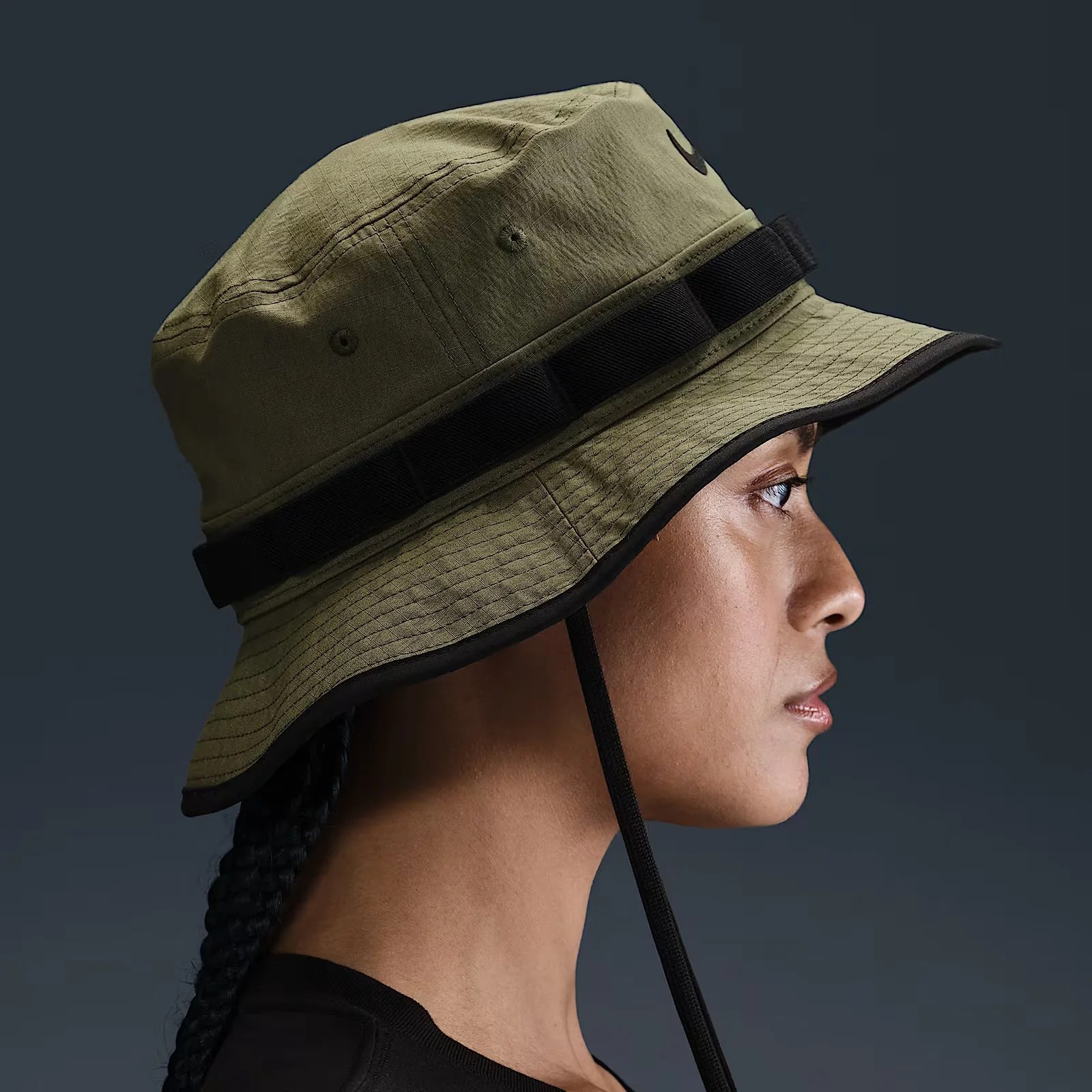 A female model shown looking to the right from the neck up wearing a Nike Apex Dri-FIT Bucket hat in medium olive.