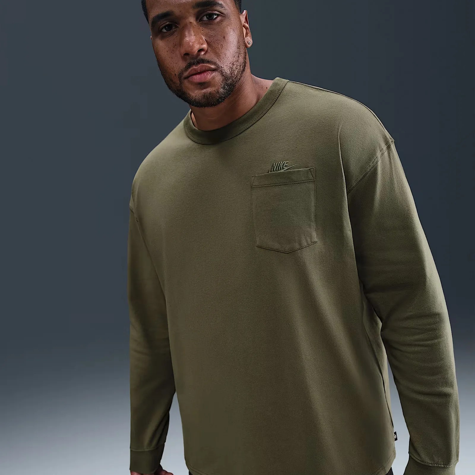 A male model shown wearing an olive green long sleeve Nike t-shirt