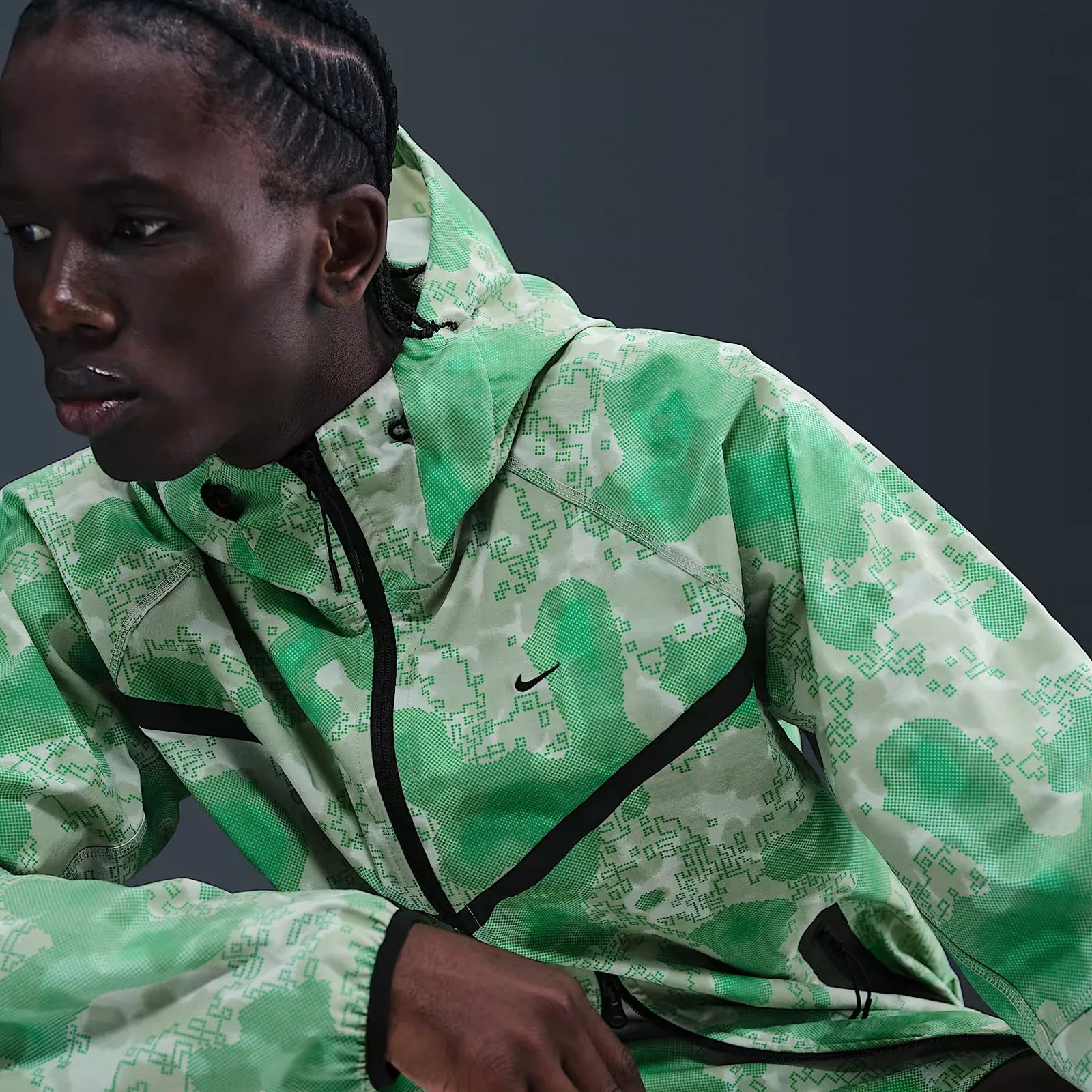 A male model shown leaning to the left of the image frame wearing a digital camo patterned Nike jacket in bright green