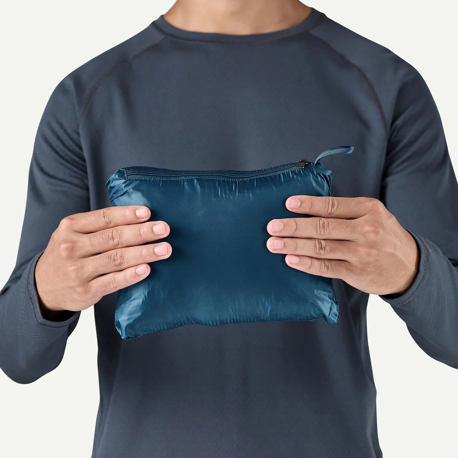 A Patagonia Nano Puff Jacket in blue shown stuffed into its own pocket stuff sack and held between two male hands