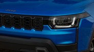 Front view of a blue Jeep vehicle showing the grille with the Jeep logo and a modern headlight design. The grille features a black honeycomb pattern, and the headlight has a distinctive LED outline. The bumper below is black with a rugged design.
