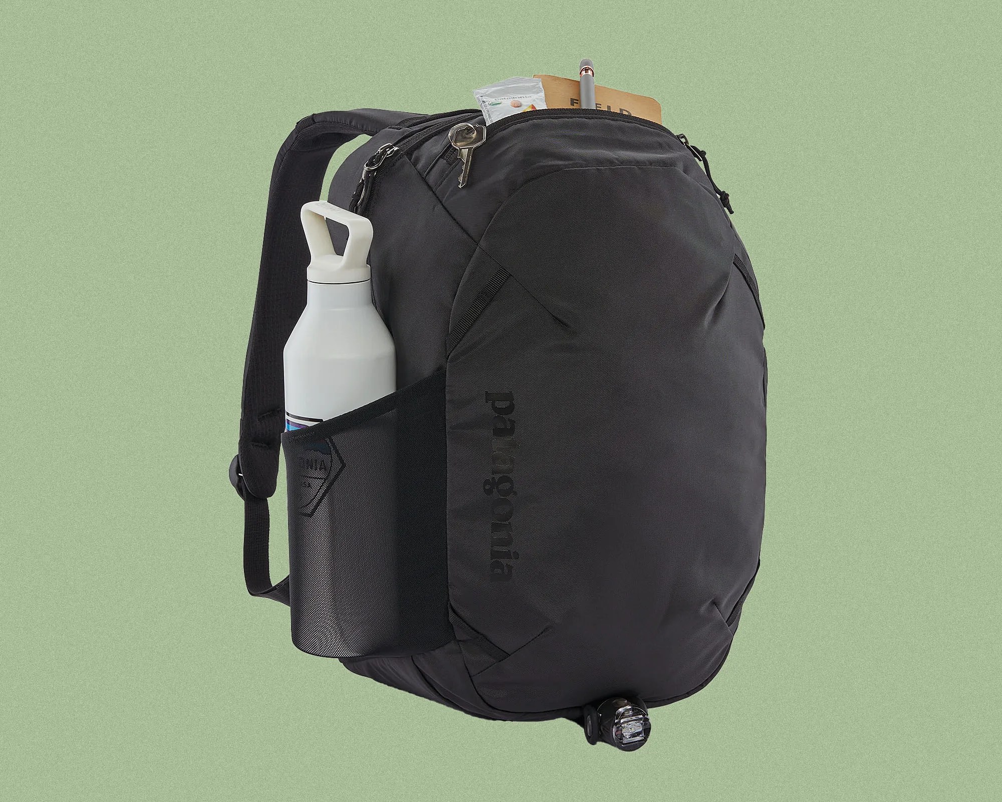 Black Patagonia backpack with a side mesh pocket holding a white water bottle, a key attached to the top zipper, and a notebook and pen partially visible in the main compartment.