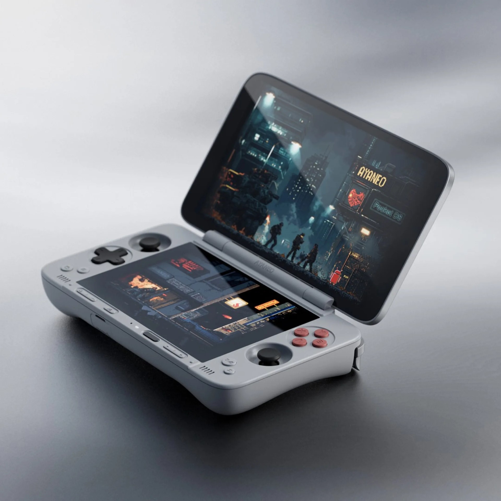 A gray handheld gaming console with a clamshell design, featuring two screens. The top screen displays a dark, futuristic cityscape with silhouettes of people and the text "AYANEO" and "Pocket DS." The bottom screen shows a similar dark city scene. The console has a directional pad and buttons on the left side, and four red buttons and a joystick on the right side.