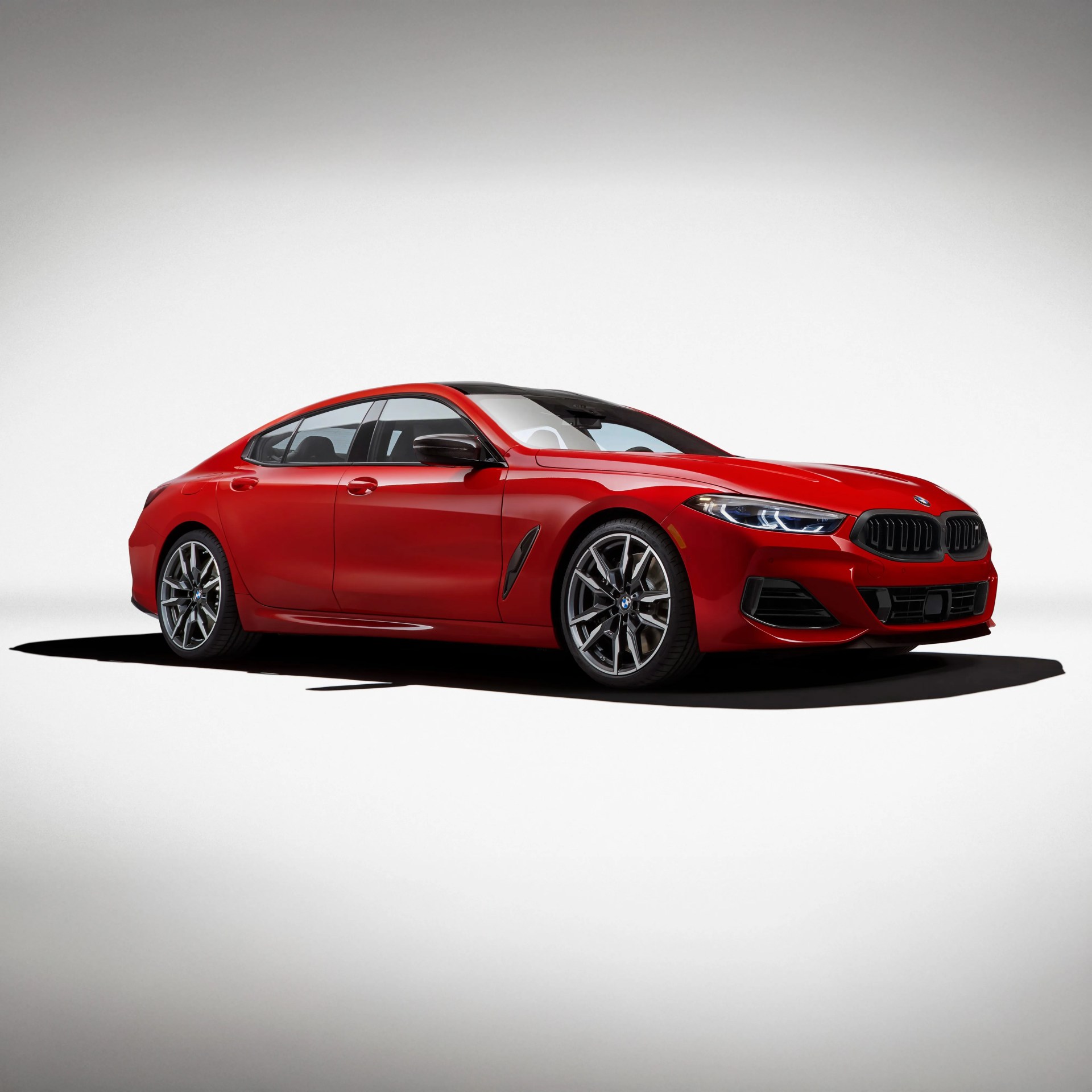 Red BMW 8 Series Gran Coupe with black kidney grilles, sleek LED headlights, and sporty alloy wheels, shown in a studio setting with a white background.