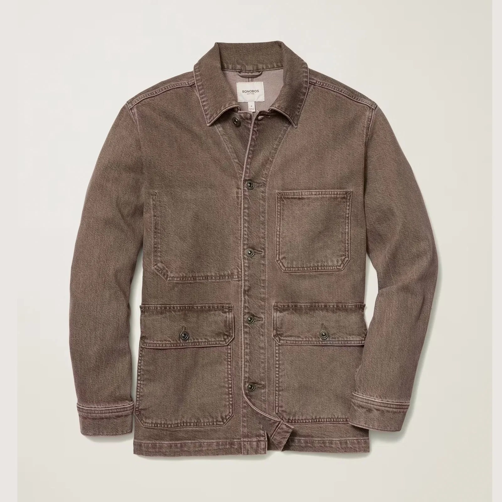 Brown denim chore jacket with a classic collar, button front closure, and four front pockets—two chest pockets and two lower flap pockets with button closures. The jacket has visible stitching details and a slightly worn, vintage look.