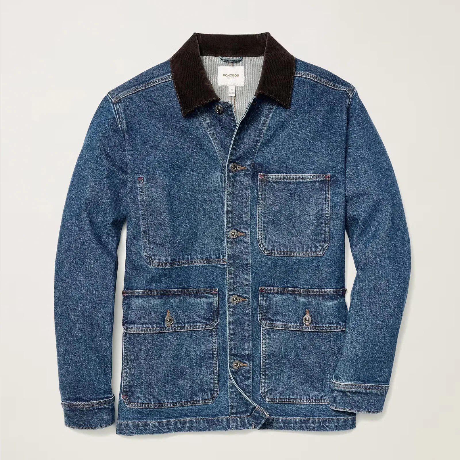 Denim jacket with a dark brown corduroy collar, featuring a button-up front and four front pockets—one chest pocket and three lower pockets, two of which have buttoned flaps. The jacket has a slightly worn look with visible stitching details.