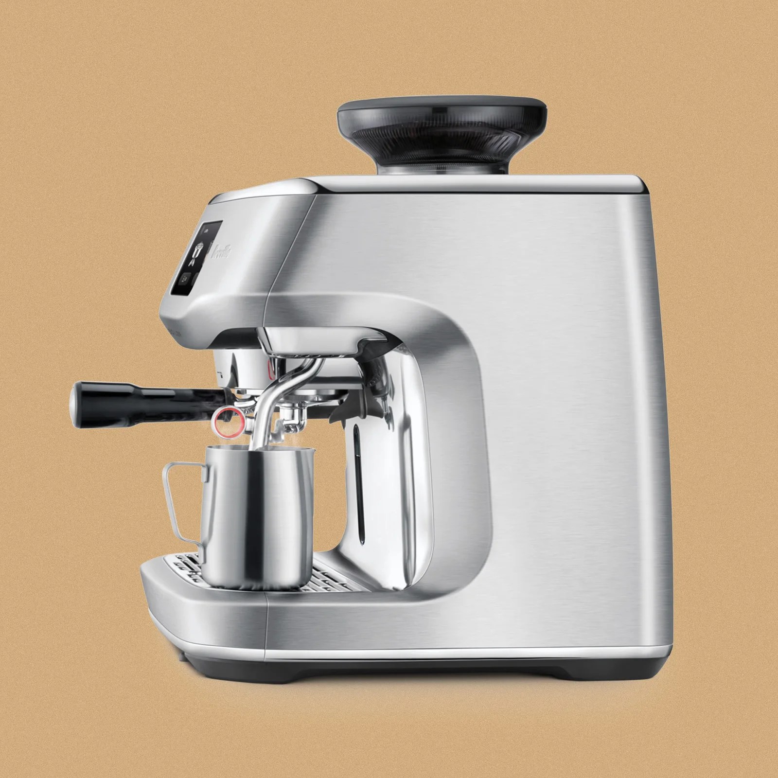 Sleek stainless steel espresso machine with a built-in grinder on top, a portafilter handle on the left side, and a metal milk frothing pitcher placed on the drip tray beneath the steam wand. The machine has a modern, compact design with a digital display on the front left side.
