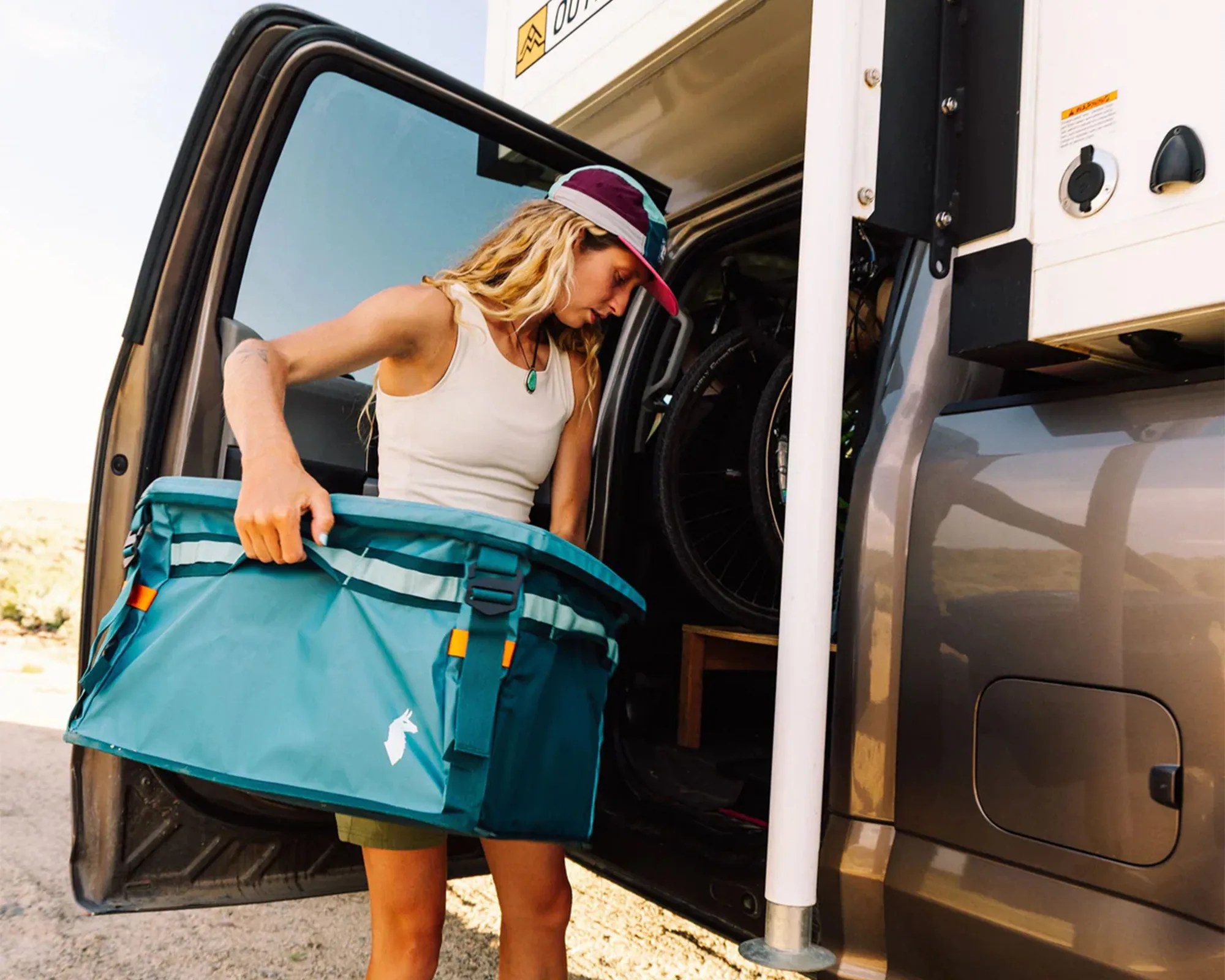 Person holding Cotopaxi Allpa 60L Gear Hauler Box next to camper truck
