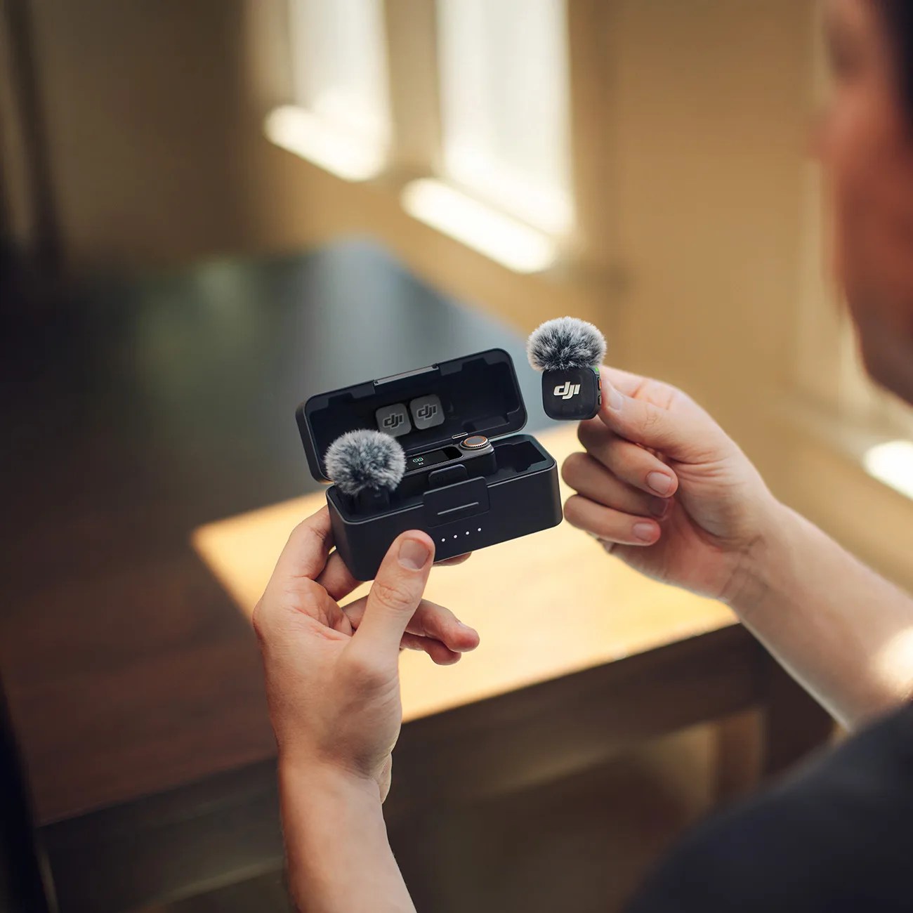 Một người cầm hai micro không dây DJI màu đen với lớp chắn gió xám