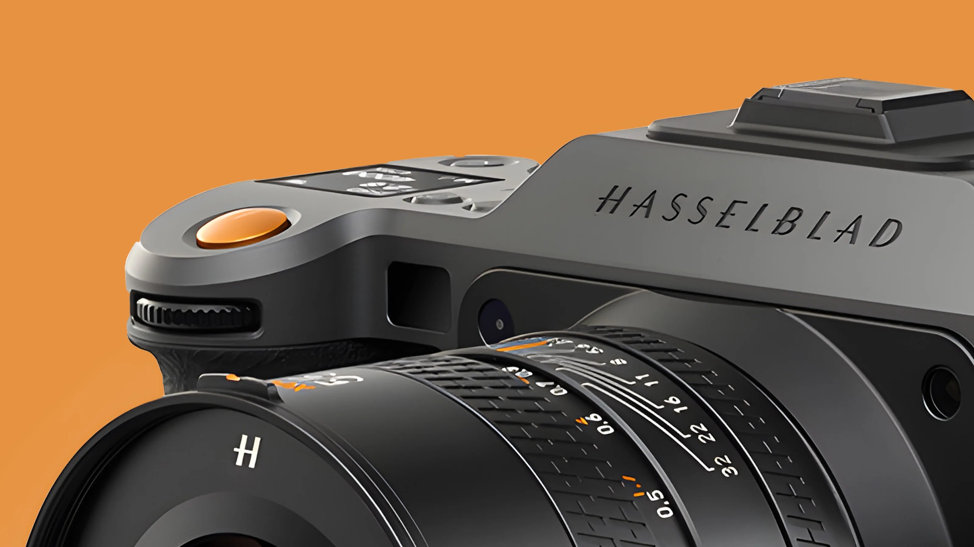 Close-up of a Hasselblad camera showing the top part with the shutter button, control dial, and part of the lens with focus and aperture markings. The camera body is gray with black and orange accents, set against an orange background.