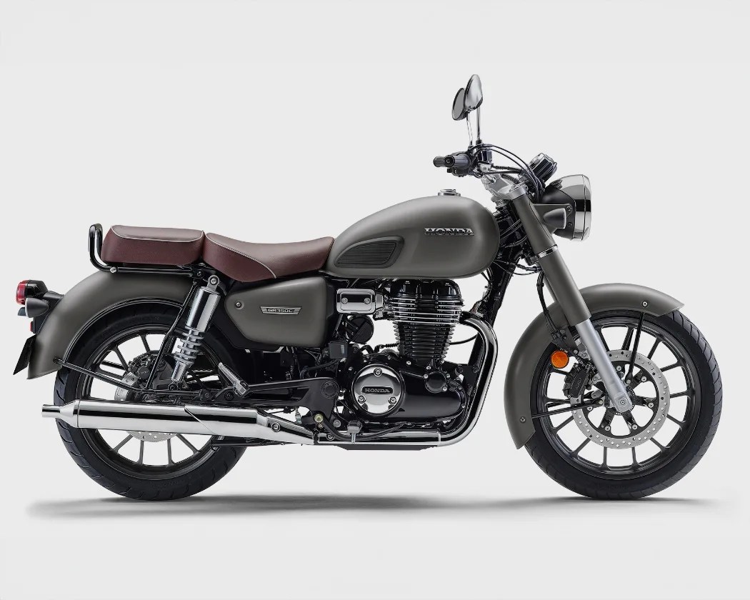 Matte gray Honda motorcycle with a classic design, featuring a brown leather seat, black engine, chrome exhaust pipe, and black alloy wheels with disc brakes.