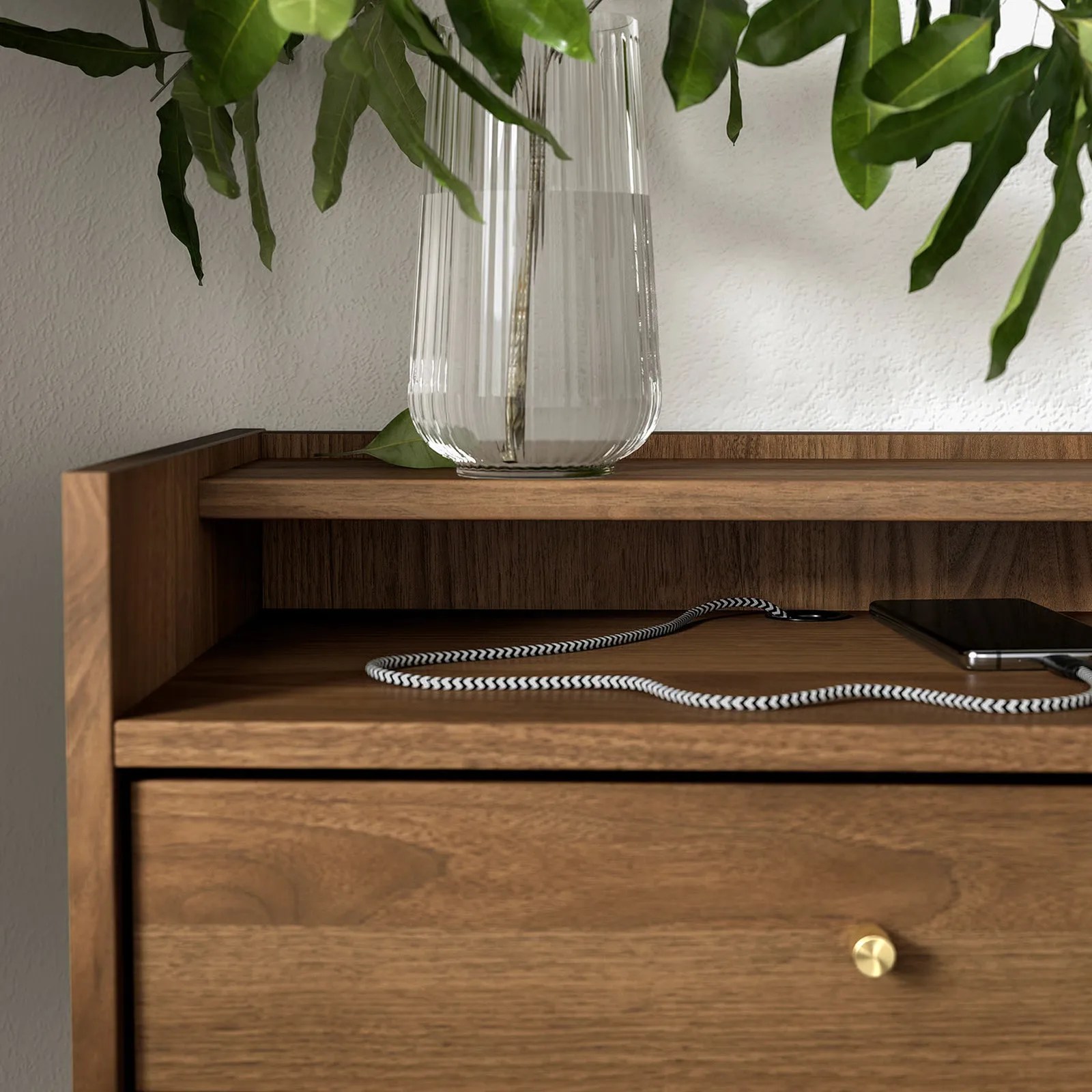 The a close-up of the IKEA-RADMANSO nightstand shown with a phone charging via an attached cable tucked into a cord run