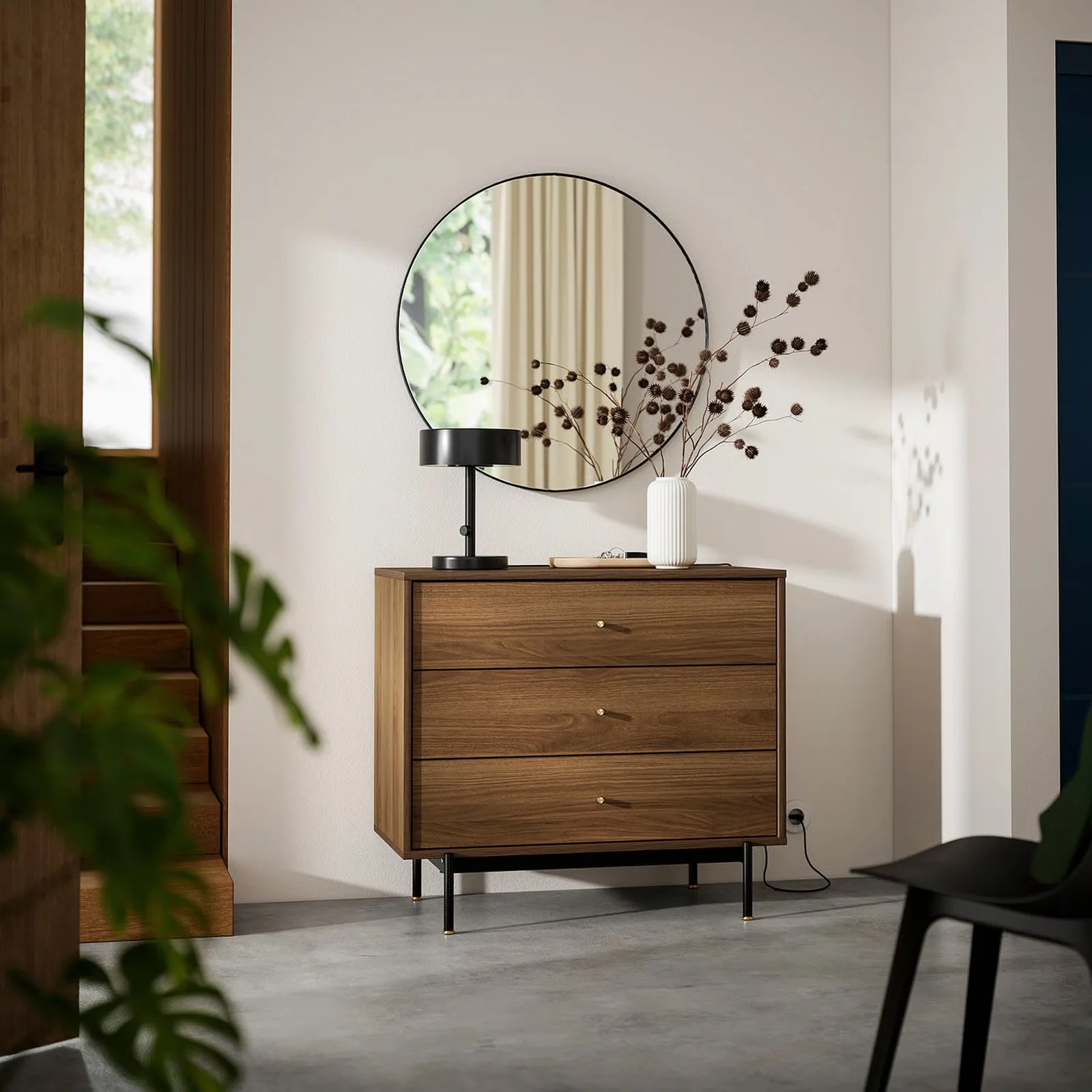 The IKEA RADMANSO three drawer dresser shown against a white wall with a circular mirror above it and an black lamp and plant on top