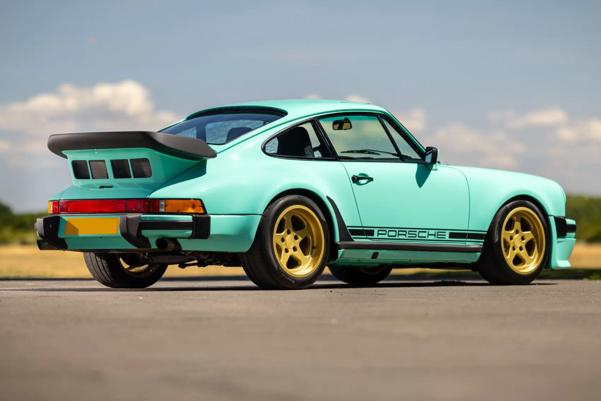 a rear photo of a mint green porsche 911 with gold wheels