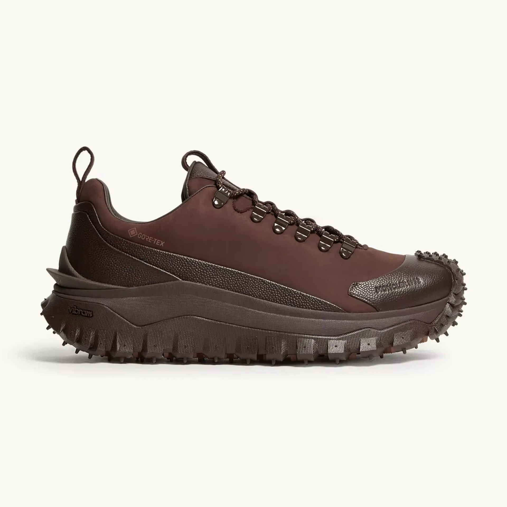 Dark brown low-top hiking shoe with a rugged Vibram sole, featuring Gore-Tex material for waterproofing. The shoe has metal eyelets for the laces, textured leather accents on the heel and toe, and pull tabs on the tongue and heel. The sole is thick with aggressive treads for traction.