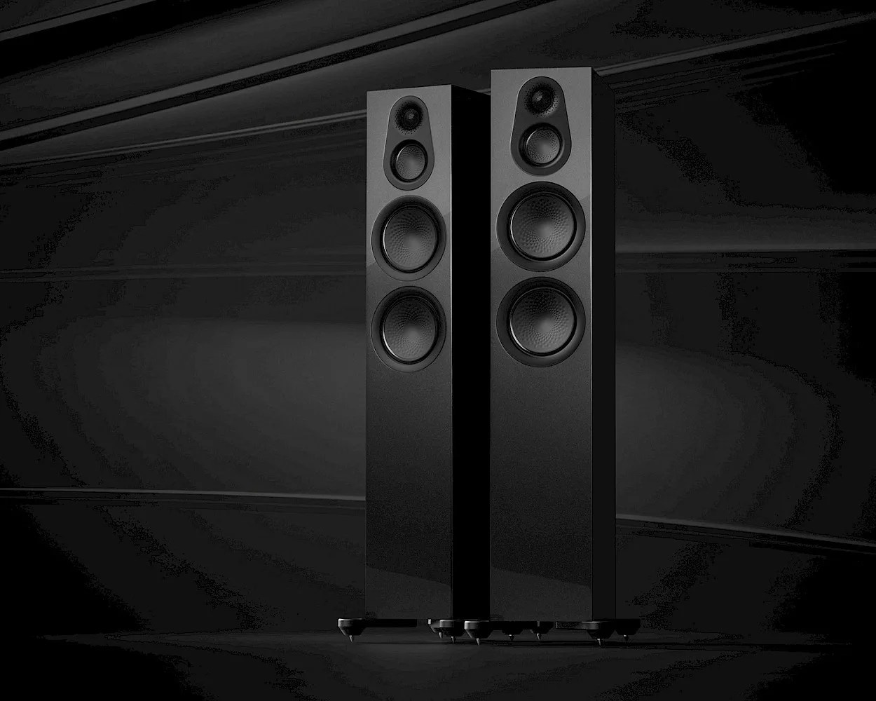 Two tall, black floor-standing speakers with a sleek, modern design, each featuring four visible drivers arranged vertically on the front panel. The speakers are set against a dark, minimalist background.
