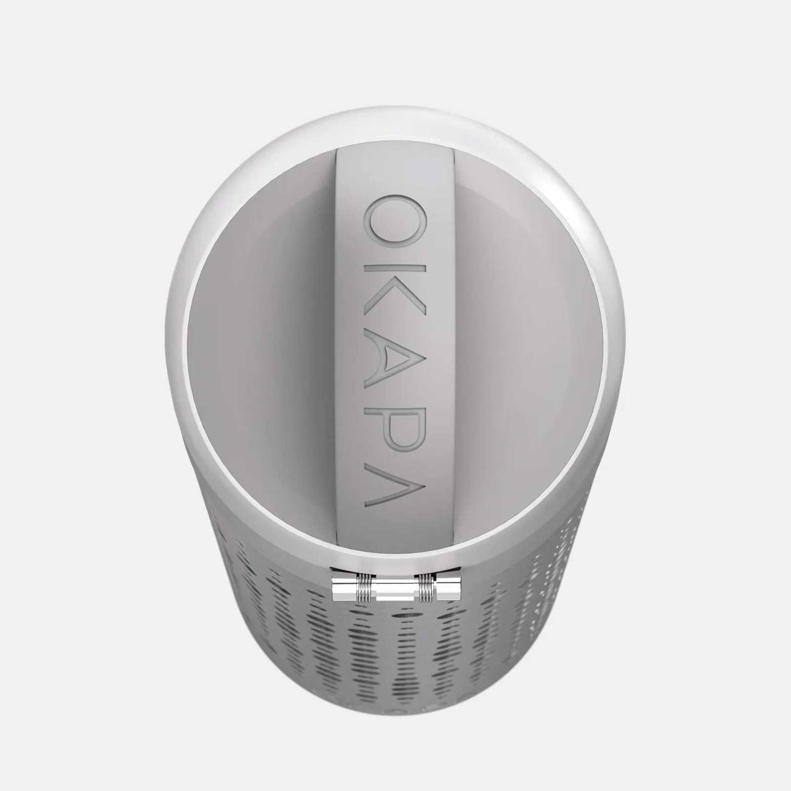 A cylindrical gray device with a perforated outer surface and a solid top featuring a central handle embossed with the word "OKAPA." The device has a metallic hinge on the side near the top.