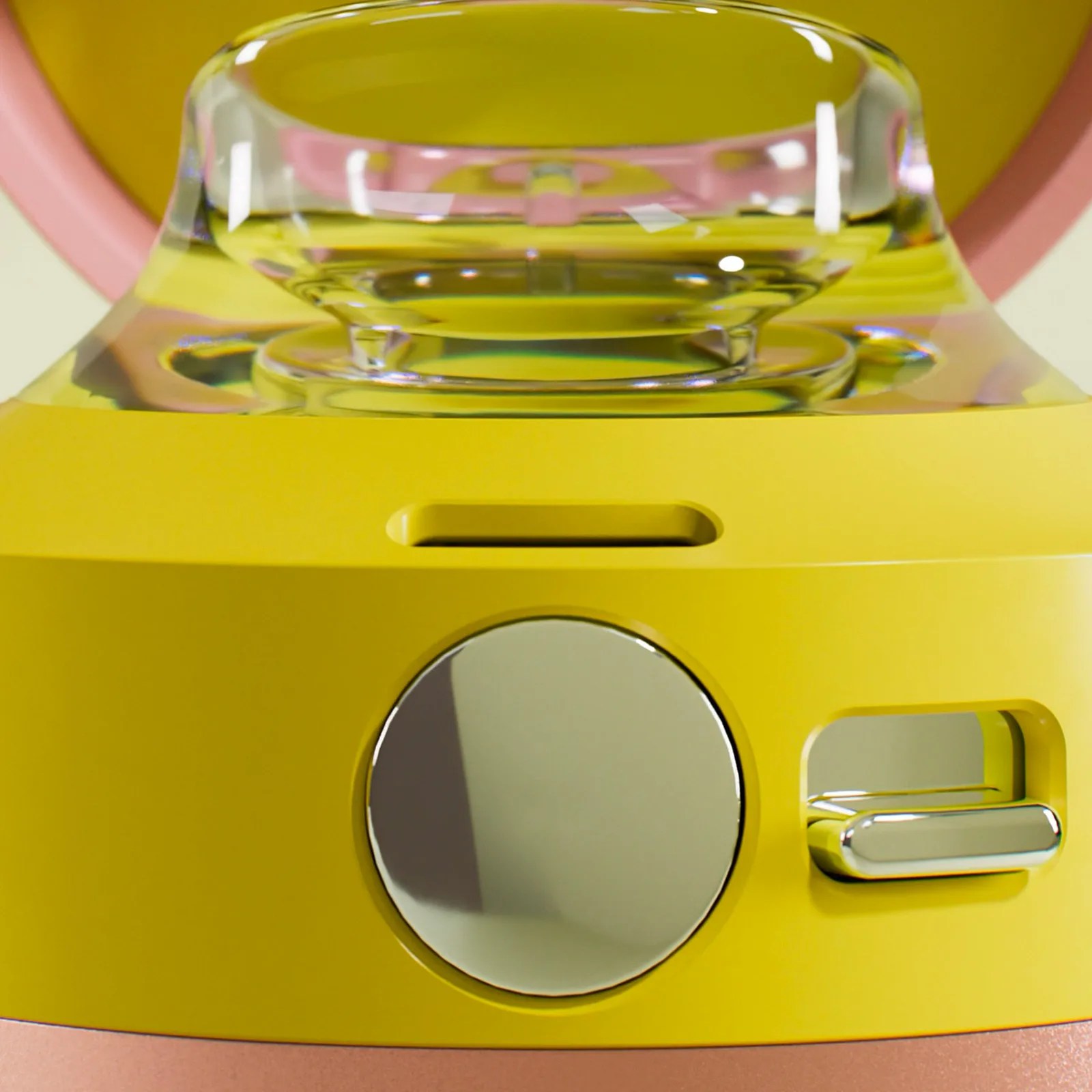 Close-up of a yellow device featuring a large circular metallic button and a smaller metallic slider switch on its front. Above these controls is a clear, rounded component, possibly a lens or a transparent button, with a pink and yellow background visible behind it. The device has a smooth, glossy finish.