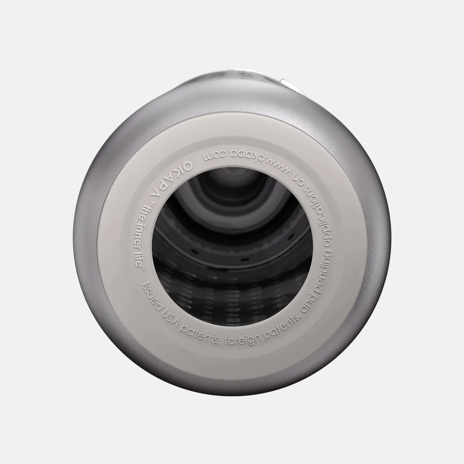 Top view of a silver-gray cylindrical object with a hollow center, featuring the text "OKAPA 'The inner life' Issued USA patents, foreign patents, and pending applications on www.okapa.com" around the inner rim. The interior appears to have a textured or patterned surface.