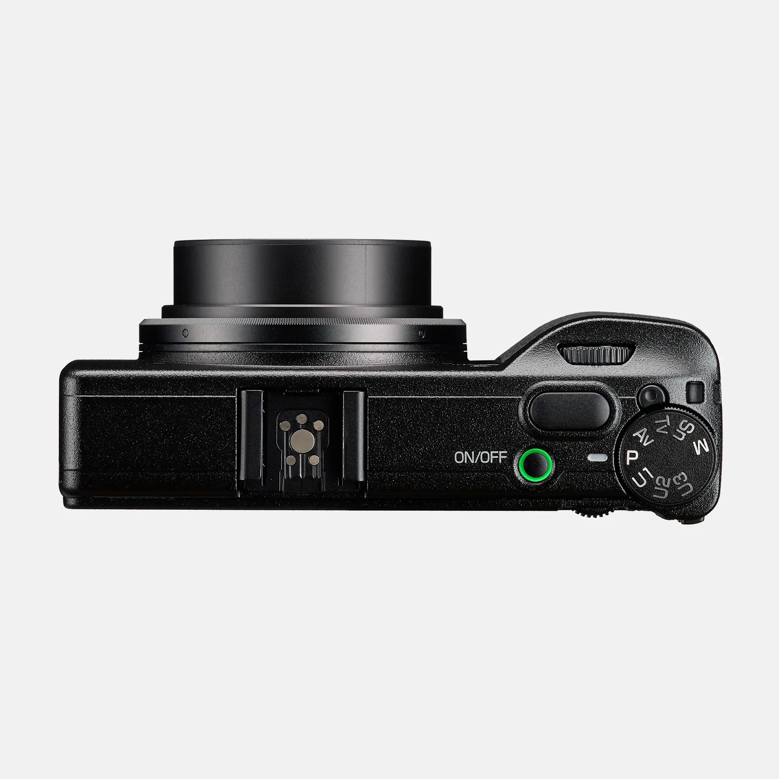 Top view of a black compact digital camera with the lens extended. The camera features an on/off button with a green ring around it, a mode dial with various settings, a shutter button, and a hot shoe mount in the center. The surface has a textured finish.