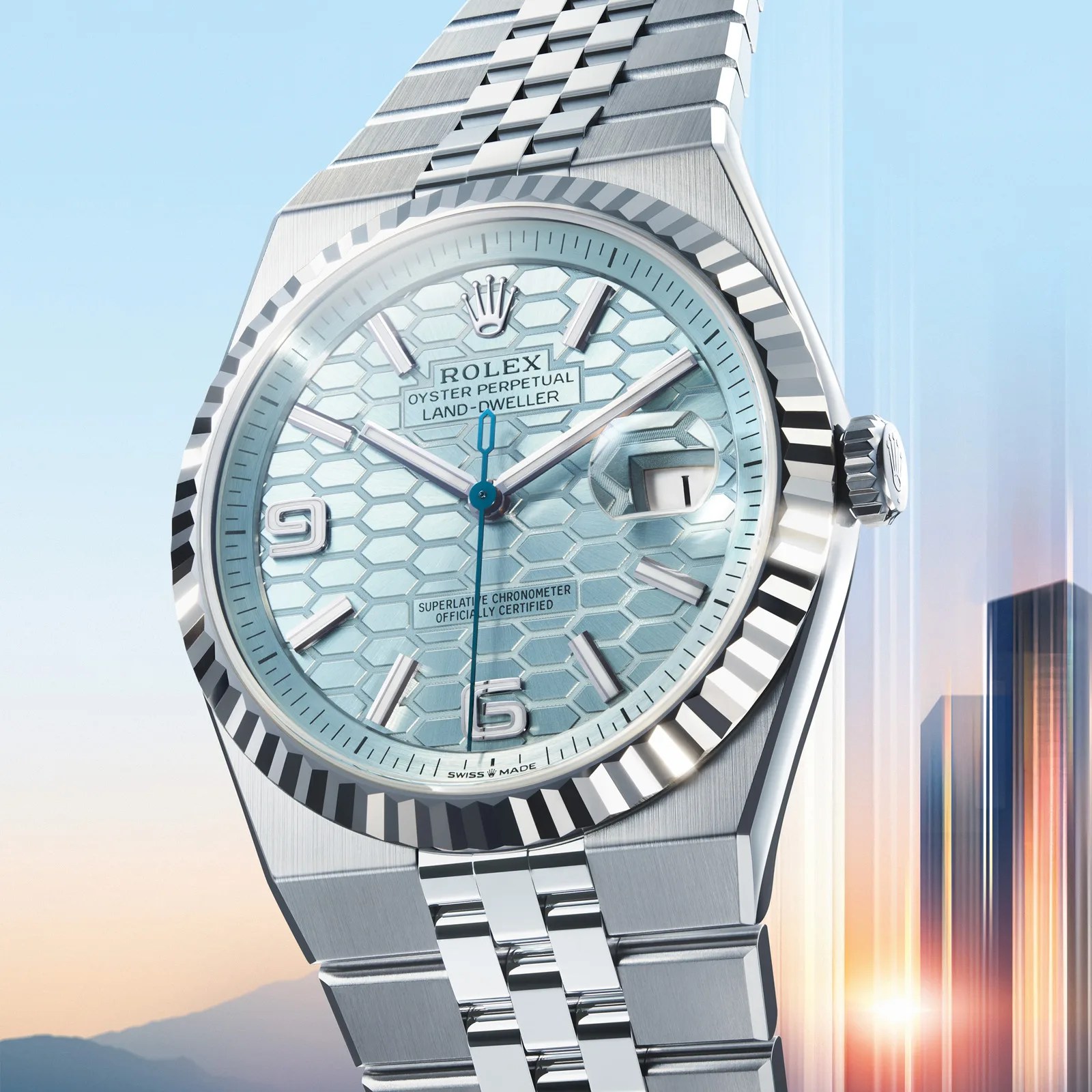 Rolex Oyster Perpetual Land-Dweller watch with a silver metal bracelet and a light blue hexagonal patterned dial. The watch features silver hour markers, a date window with a magnifier at 3 o'clock, and a blue second hand. The bezel is fluted, and the crown displays the Rolex logo. The background shows a gradient sky with a sunrise and blurred cityscape.