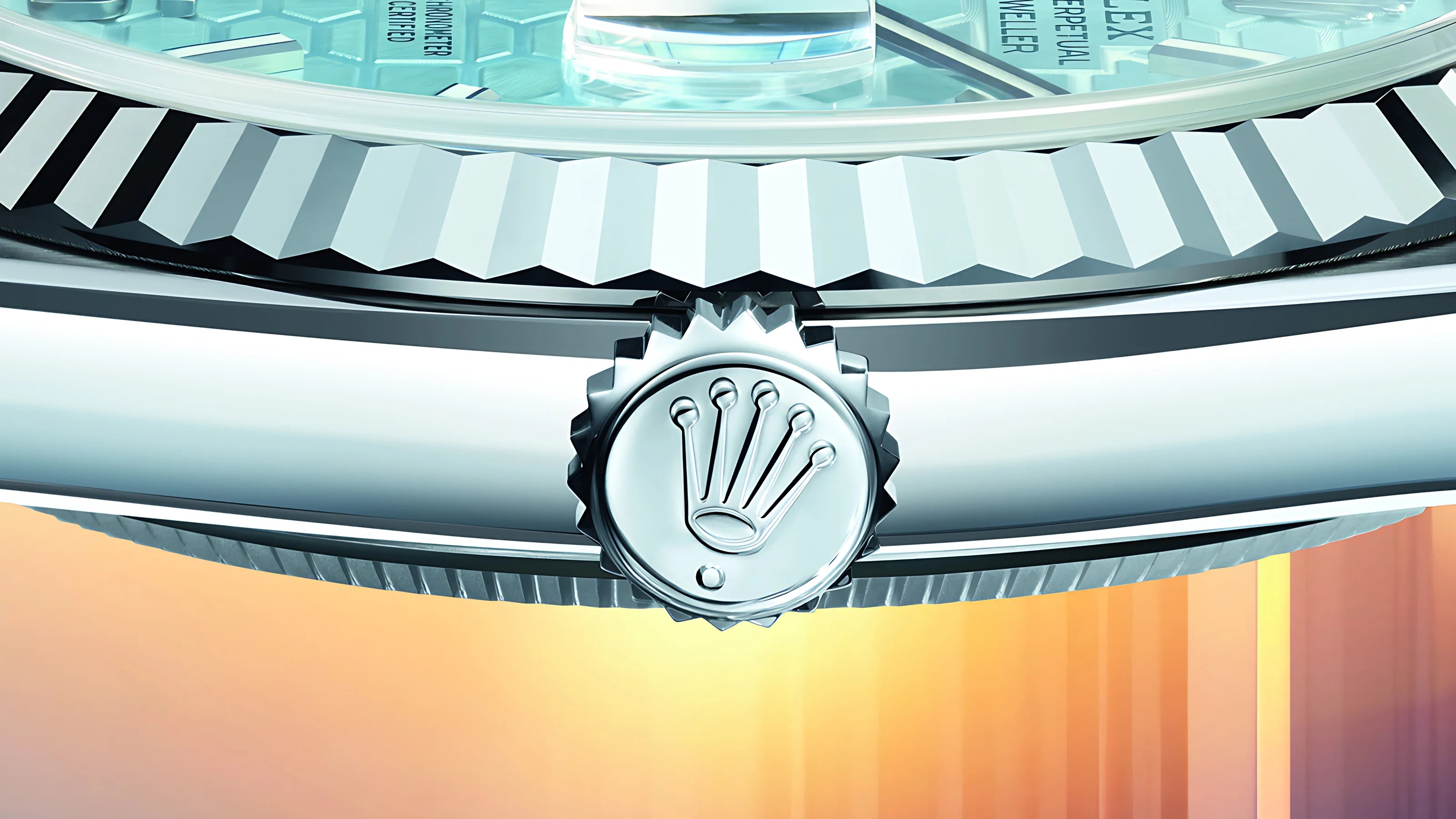 Close-up of a silver Rolex watch crown with the Rolex logo prominently displayed. The watch bezel features a fluted design, and part of the light blue watch face with text is visible above the crown. The background has a gradient of warm colors, transitioning from orange to purple.